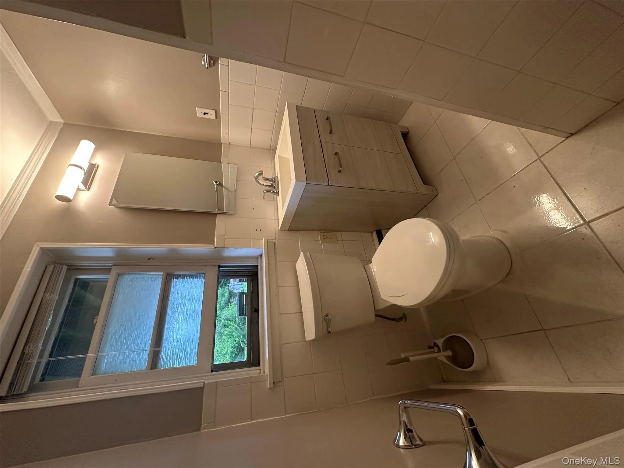 Bathroom featuring light tile patterned flooring, vanity, ornamental molding, tile walls, and a wainscoted wall Bathroom featuring light tile patterned flooring, vanity, ornamental molding, tile walls, and a wainscoted wall