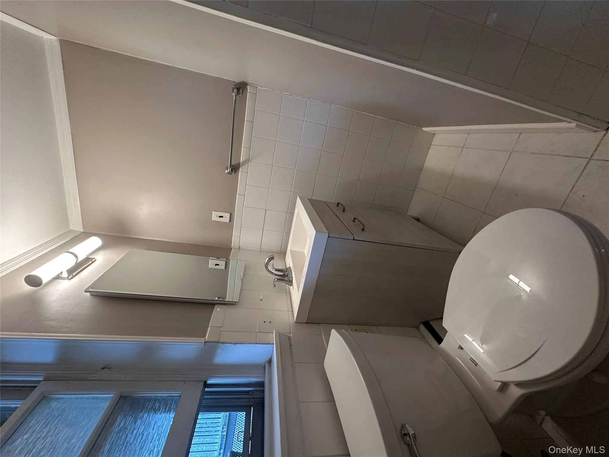 Bathroom with crown molding, vanity, tile walls, light tile patterned flooring, and a wainscoted wall Bathroom with crown molding, vanity, tile walls, light tile patterned flooring, and a wainscoted wall