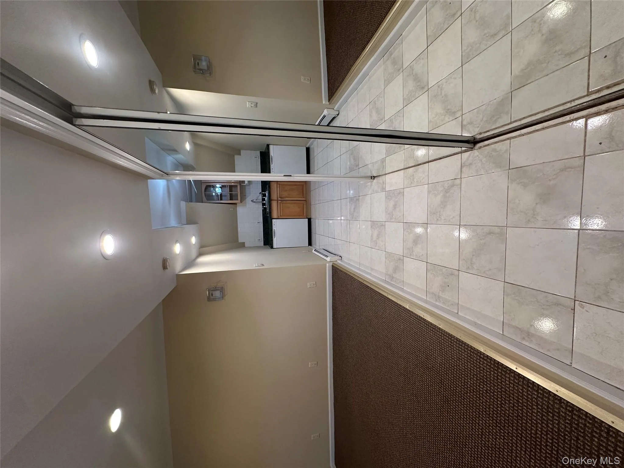 Hallway featuring light tile patterned floors, recessed lighting, light carpet, and a baseboard radiator Hallway featuring light tile patterned floors, recessed lighting, light carpet, and a baseboard radiator