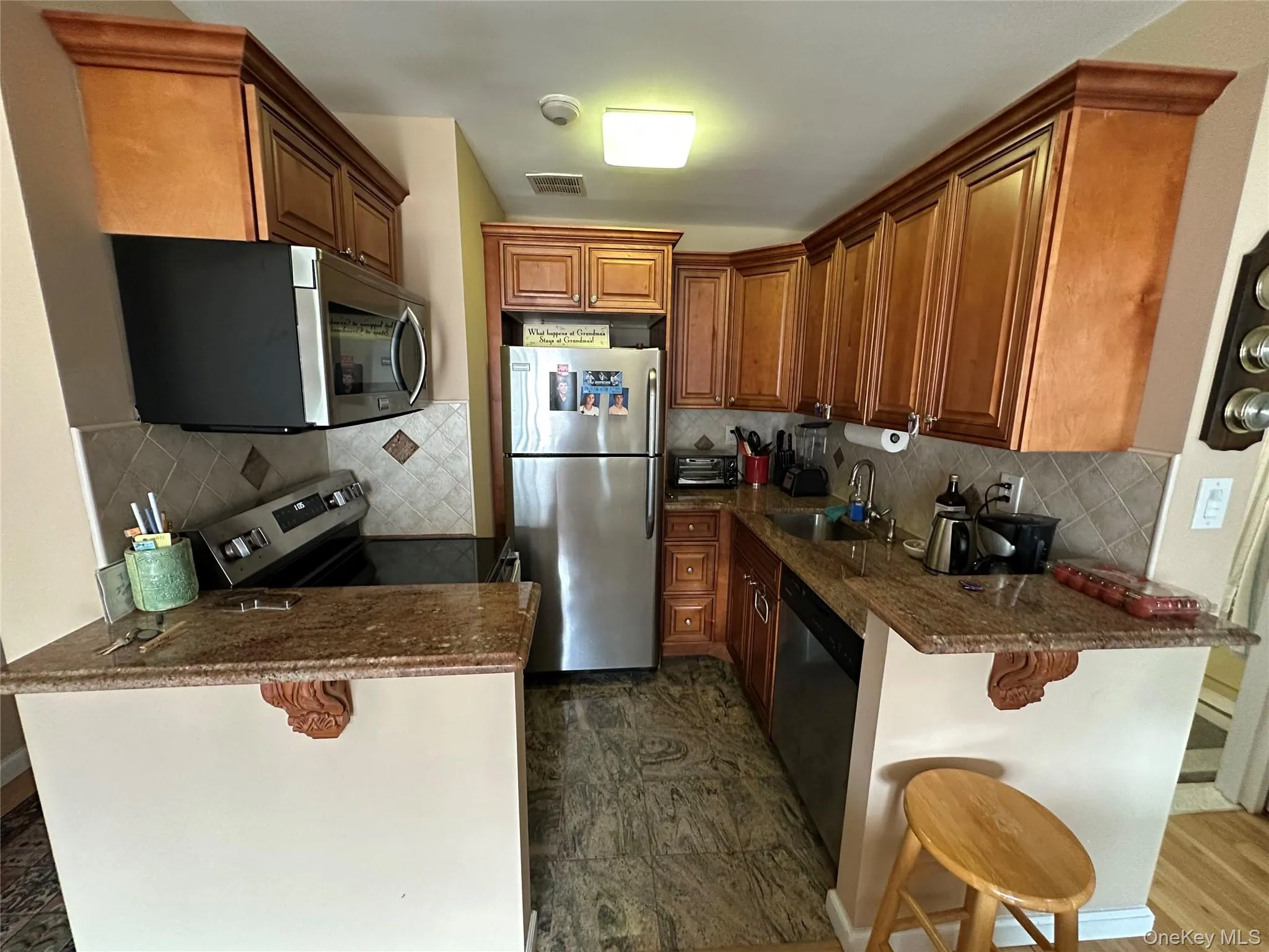 Kitchen with a peninsula, a kitchen breakfast bar, stainless steel appliances, decorative backsplash, and dark stone countertops Kitchen with a peninsula, a kitchen breakfast bar, stainless steel appliances, decorative backsplash, and dark stone countertops
