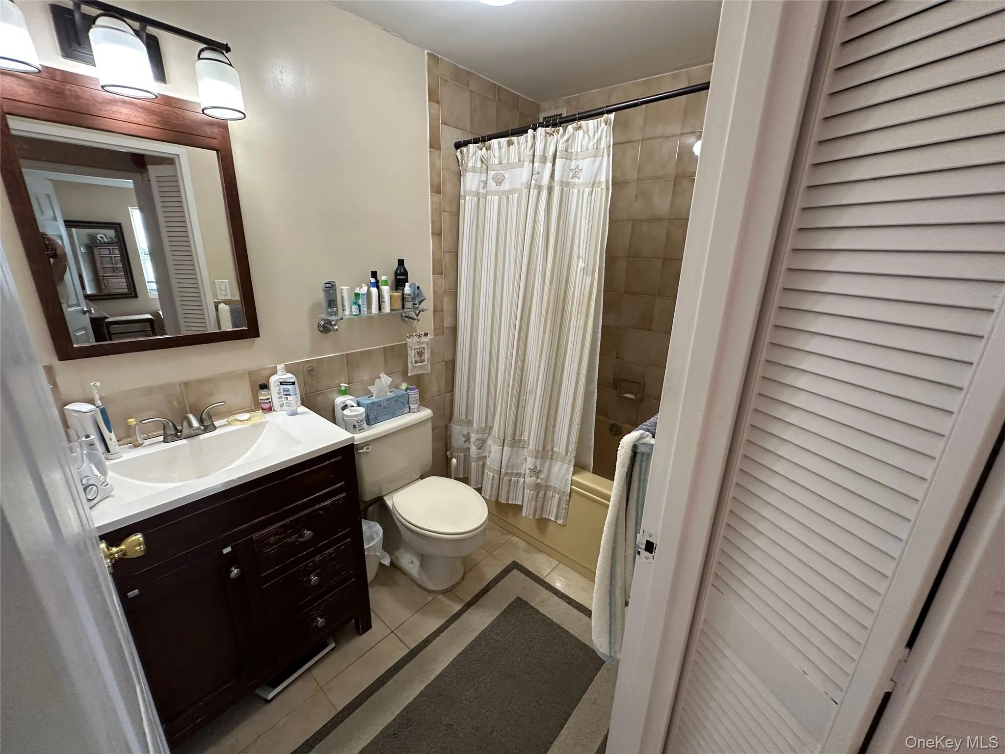 Bathroom featuring a closet, light tile patterned floors, shower / bath combo with shower curtain, and tile walls Bathroom featuring a closet, light tile patterned floors, shower / bath combo with shower curtain, and tile walls