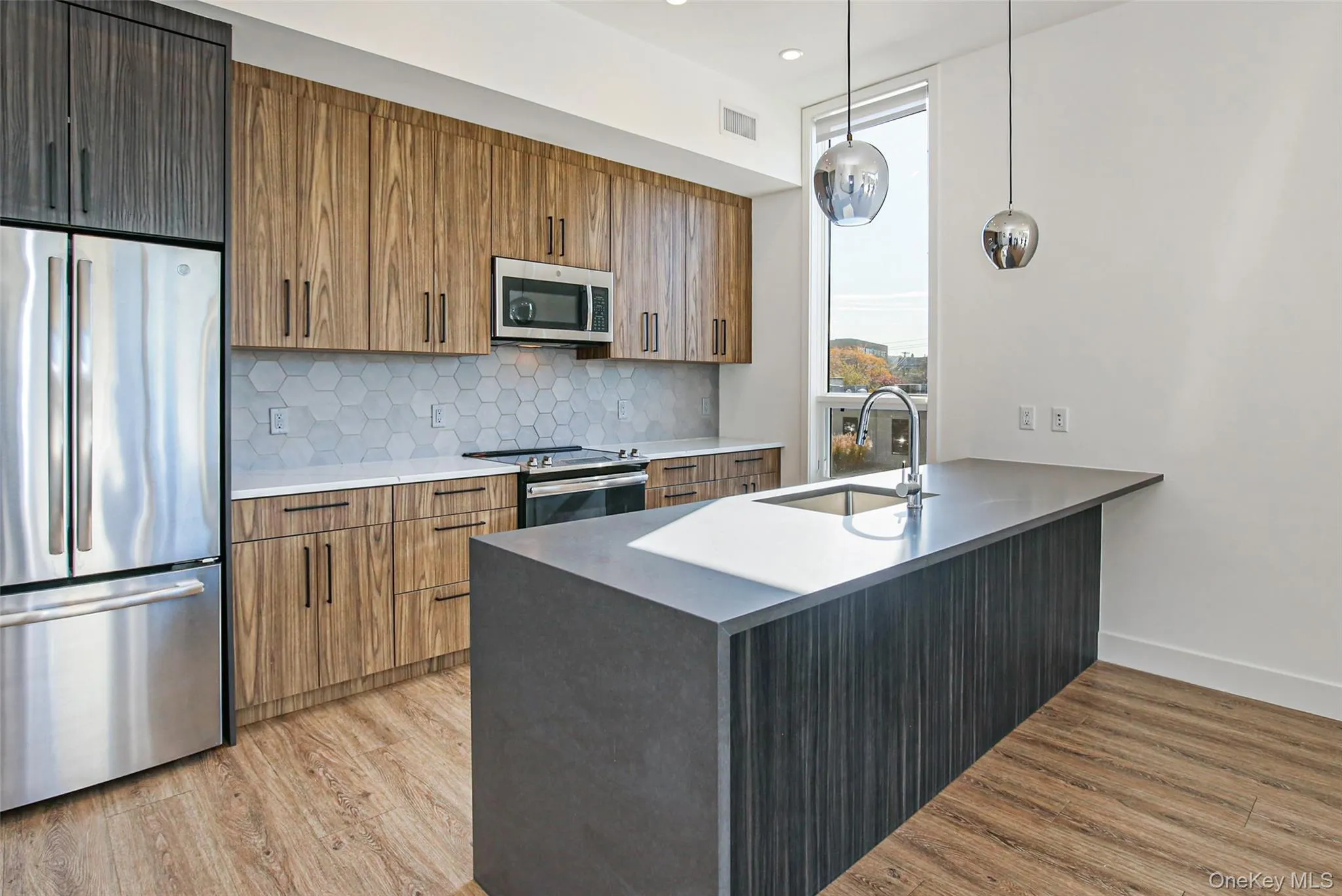 Kitchen with sink, appliances with stainless steel finishes, backsplash, hanging light fixtures, and light hardwood / wood-style floors Kitchen with sink, appliances with stainless steel finishes, backsplash, hanging light fixtures, and light hardwood / wood-style floors