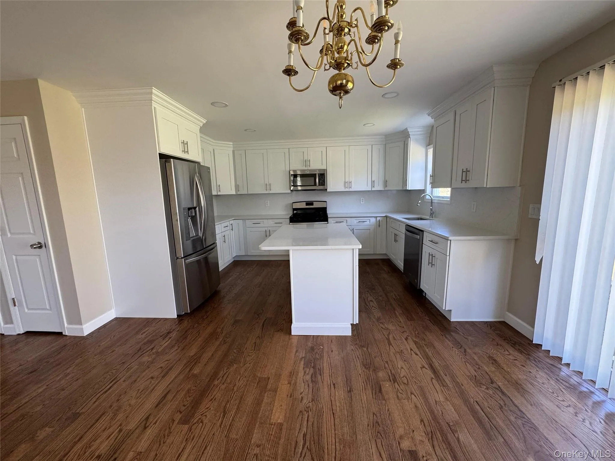 Kitchen featuring an island, white cabinetry, stainless steel appliances, and wood-finish flooring. Kitchen featuring an island, white cabinetry, stainless steel appliances, and wood-finish flooring.