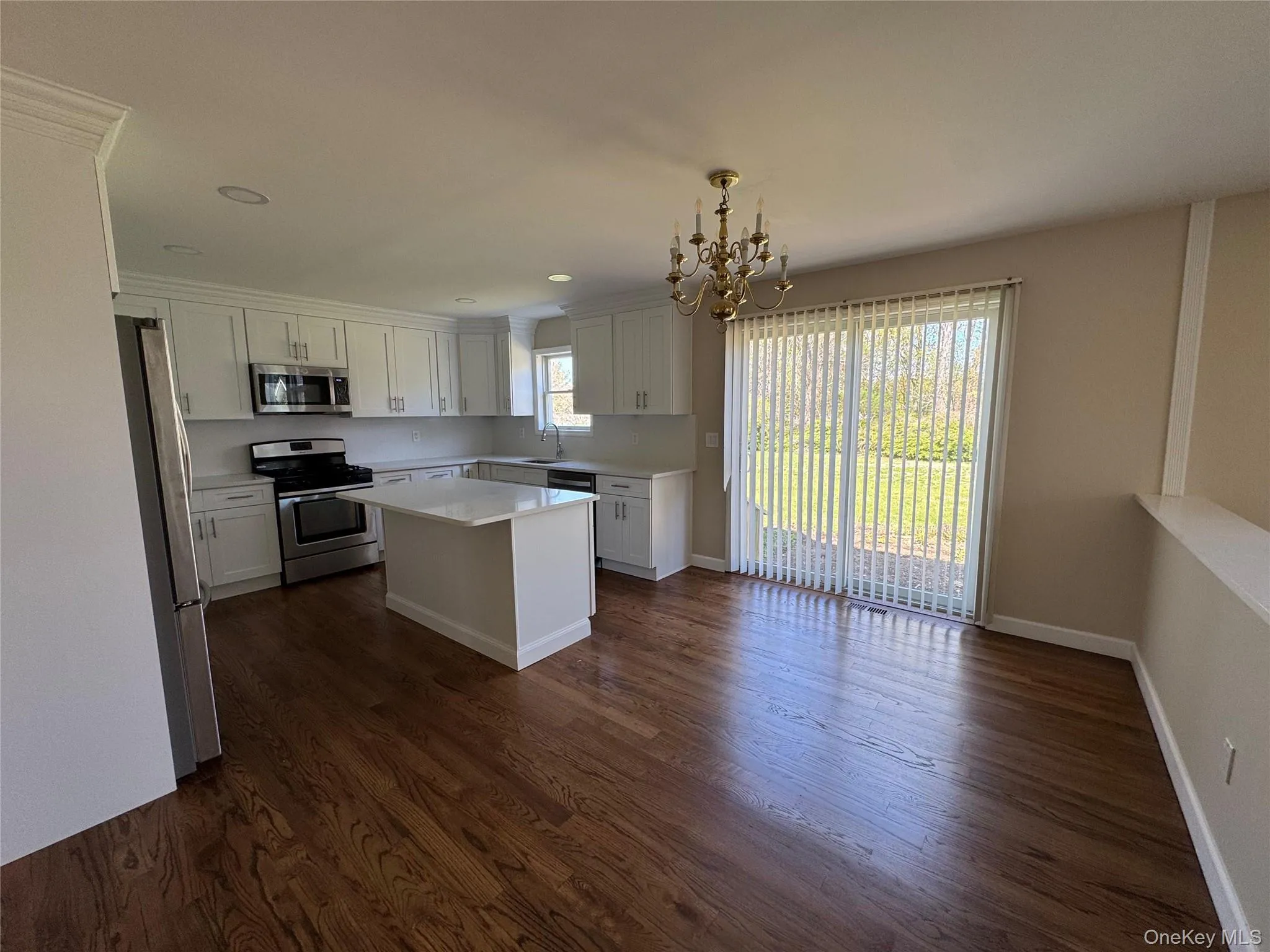 Kitchen featuring an island, white cabinetry, stainless steel appliances, and wood-finish flooring. Kitchen featuring an island, white cabinetry, stainless steel appliances, and wood-finish flooring.