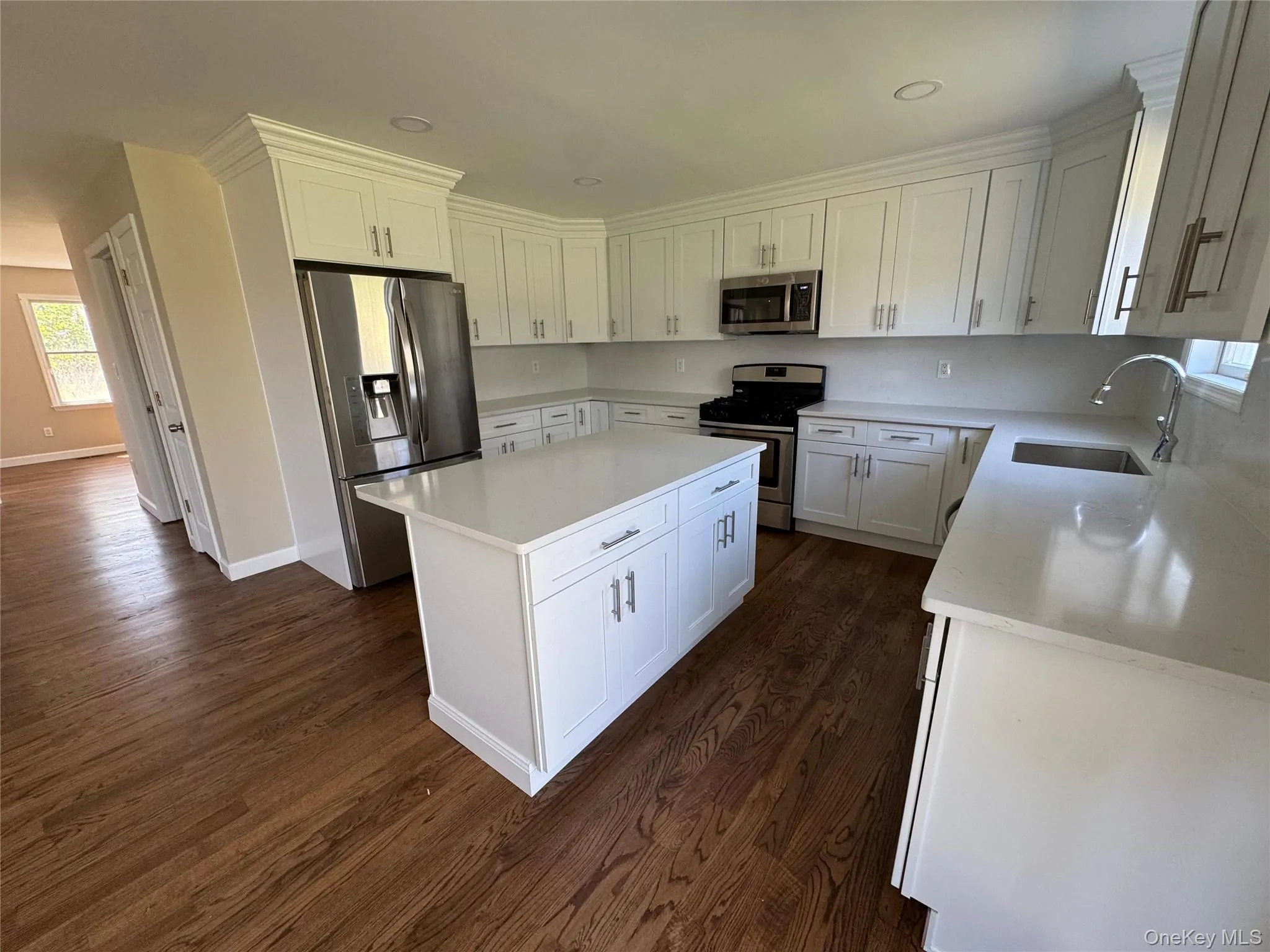 Kitchen featuring an island, white cabinetry, stainless steel appliances, and wood-finish flooring. Kitchen featuring an island, white cabinetry, stainless steel appliances, and wood-finish flooring.