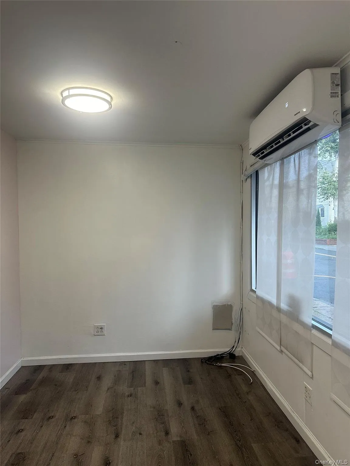 Empty room featuring dark wood-type flooring, a wall mounted AC, and crown molding Empty room featuring dark wood-type flooring, a wall mounted AC, and crown molding