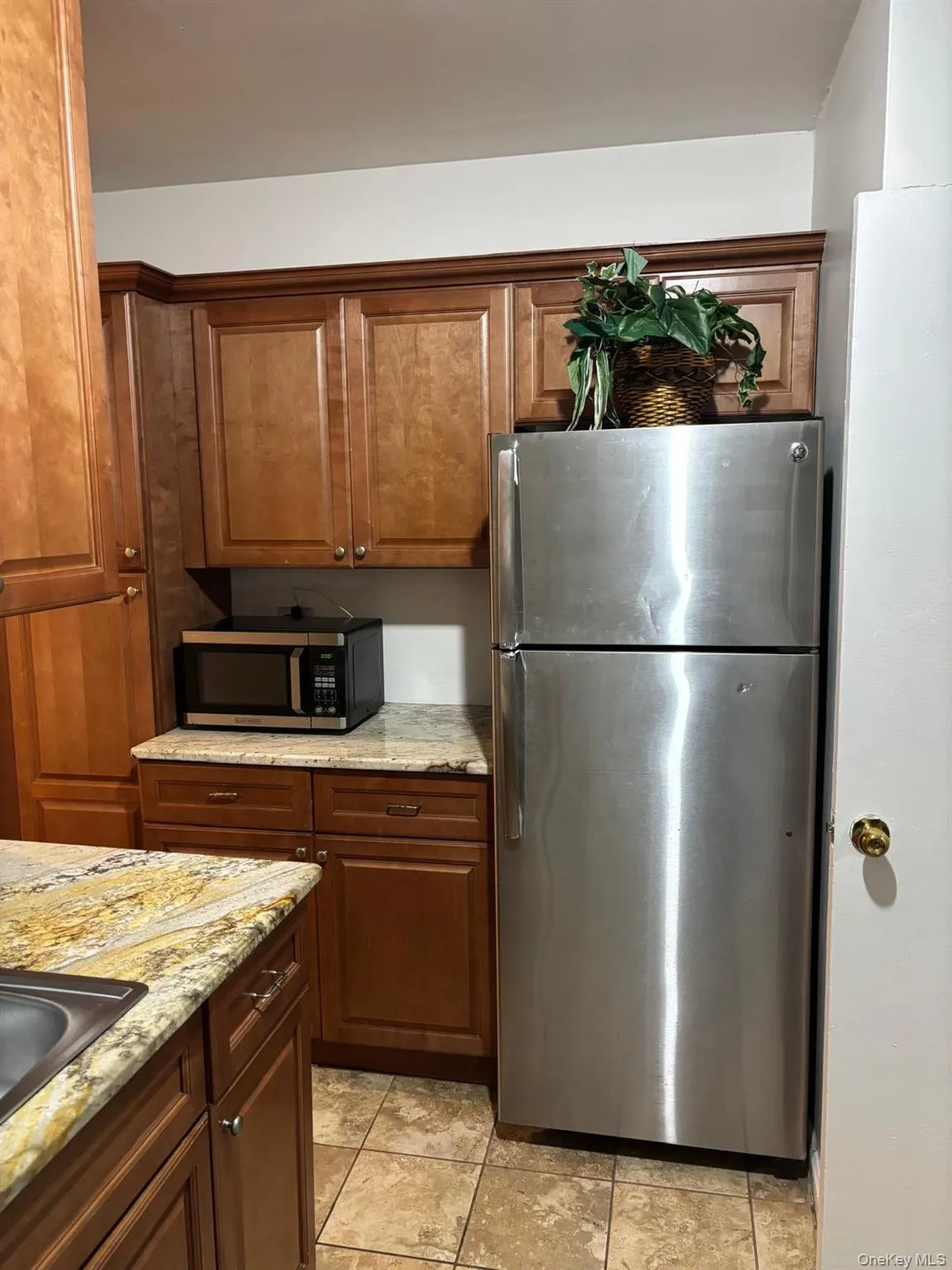 Kitchen with stainless steel appliances, light stone countertops, light tile patterned flooring, and brown cabinets Kitchen with stainless steel appliances, light stone countertops, light tile patterned flooring, and brown cabinets