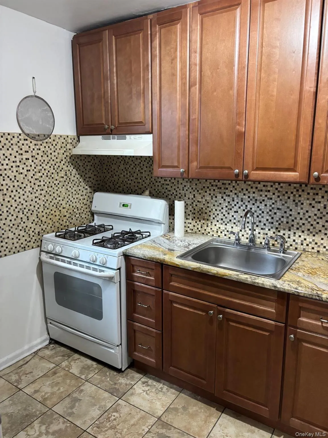 Kitchen with gas range gas stove, decorative backsplash, under cabinet range hood, light stone countertops, and light tile patterned floors Kitchen with gas range gas stove, decorative backsplash, under cabinet range hood, light stone countertops, and light tile patterned floors