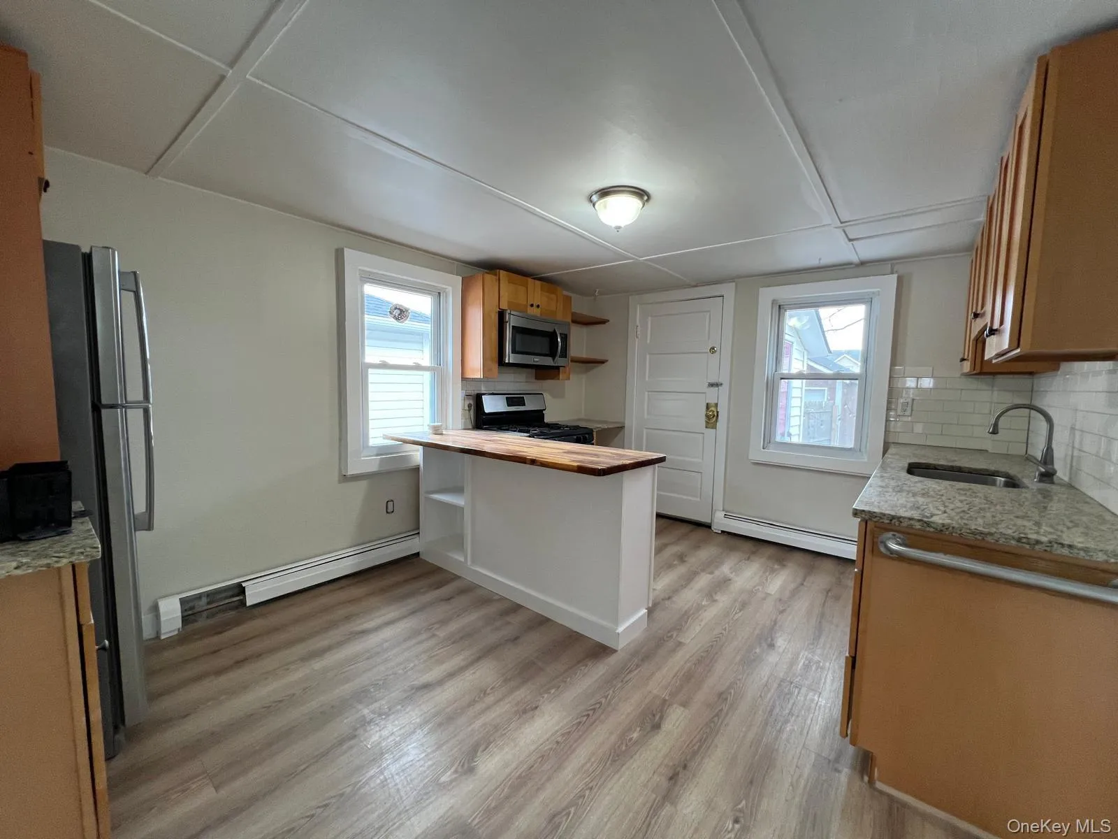 Kitchen with brown cabinetry, light stone countertops, decorative backsplash, and open shelves Kitchen with brown cabinetry, light stone countertops, decorative backsplash, and open shelves