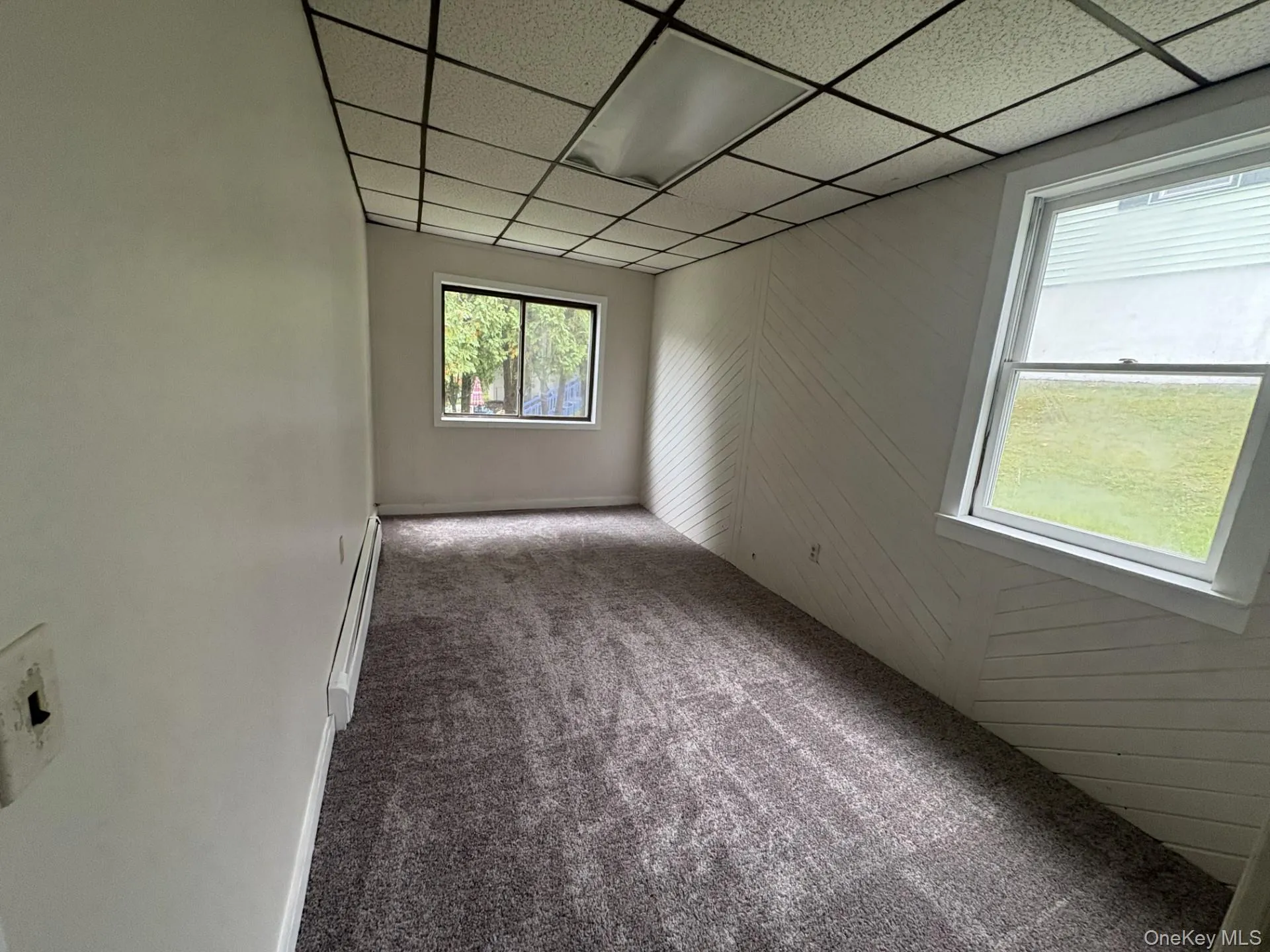 Spare room with dark colored carpet, a drop ceiling, and a baseboard radiator Spare room with dark colored carpet, a drop ceiling, and a baseboard radiator