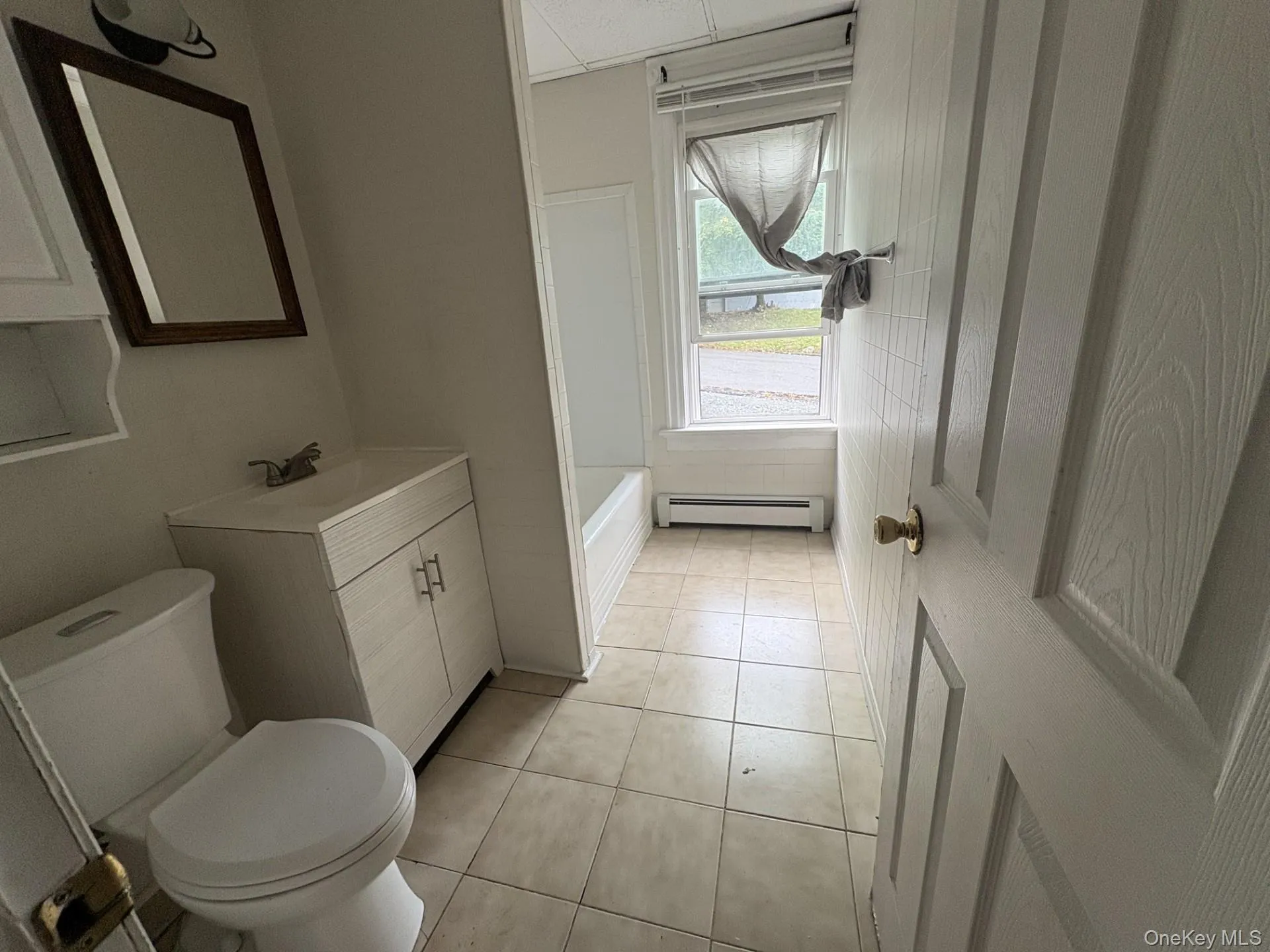 Bathroom featuring vanity, light tile patterned flooring, a bath, and baseboard heating Bathroom featuring vanity, light tile patterned flooring, a bath, and baseboard heating
