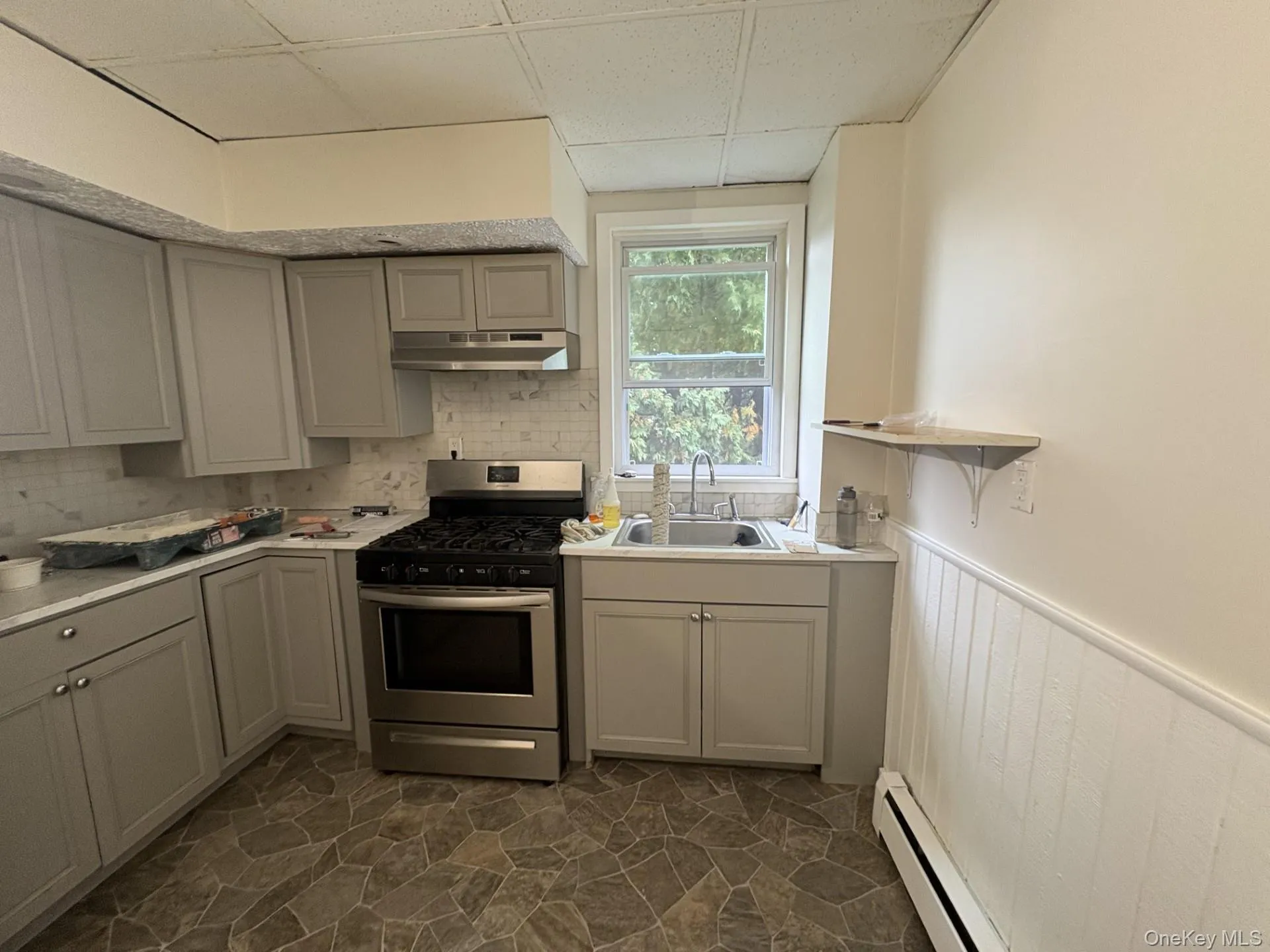 Kitchen with stainless steel range with gas stovetop, a drop ceiling, baseboard heating, wainscoting, and light countertops Kitchen with stainless steel range with gas stovetop, a drop ceiling, baseboard heating, wainscoting, and light countertops