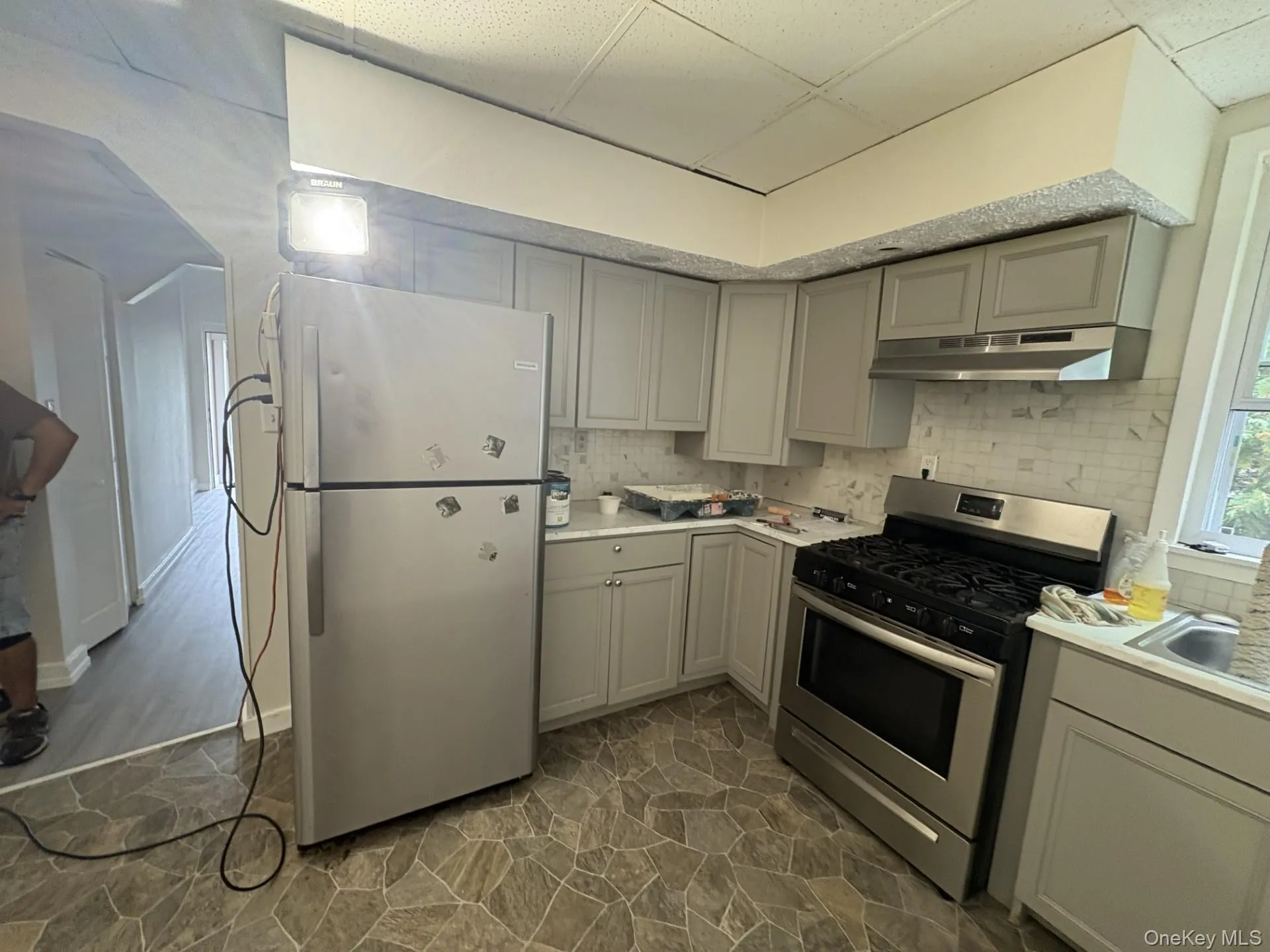 Kitchen with gray cabinetry, tasteful backsplash, stainless steel appliances, light countertops, and a drop ceiling Kitchen with gray cabinetry, tasteful backsplash, stainless steel appliances, light countertops, and a drop ceiling