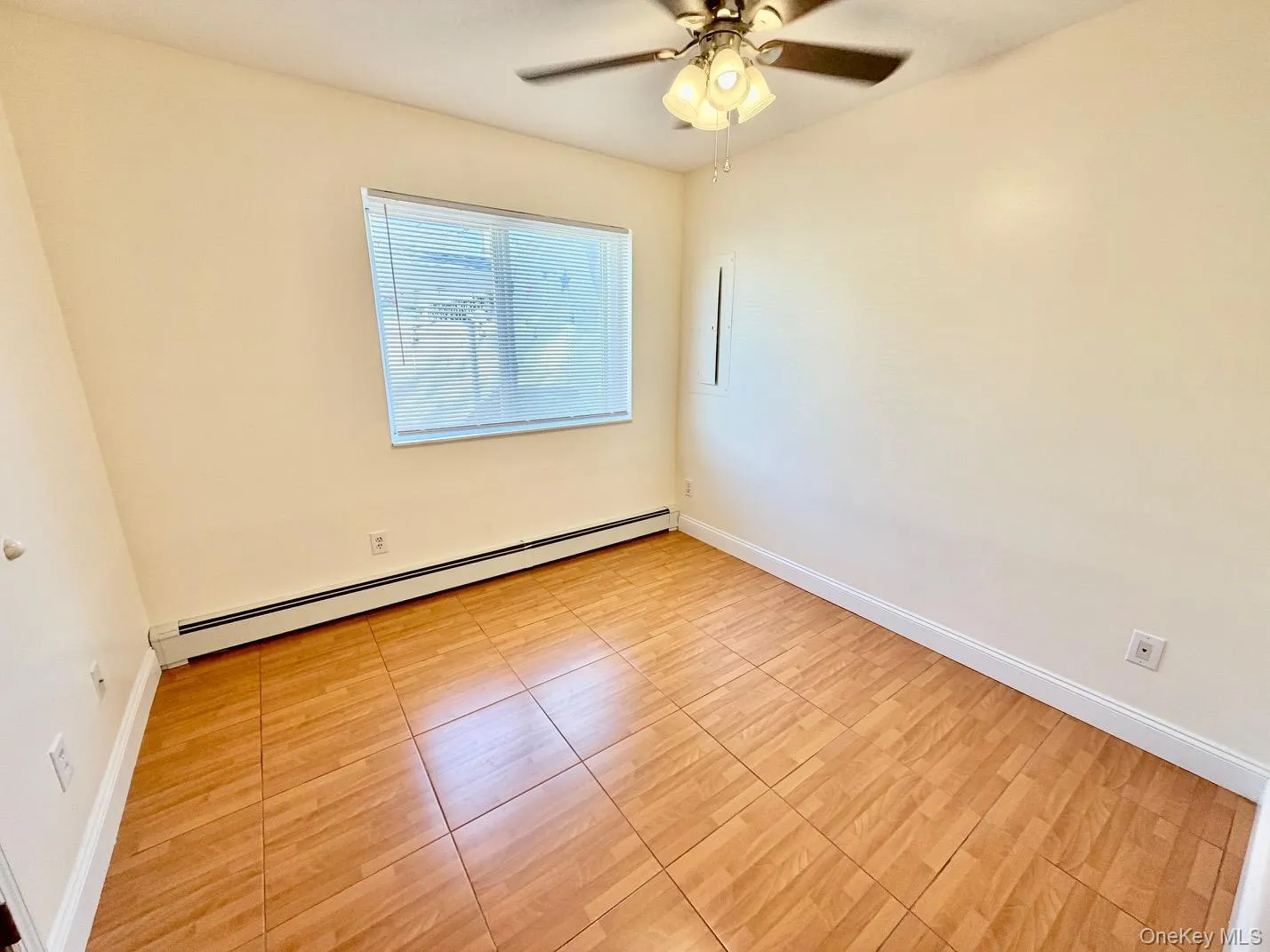 Empty room with baseboard heating, light tile patterned floors, and a ceiling fan Empty room with baseboard heating, light tile patterned floors, and a ceiling fan
