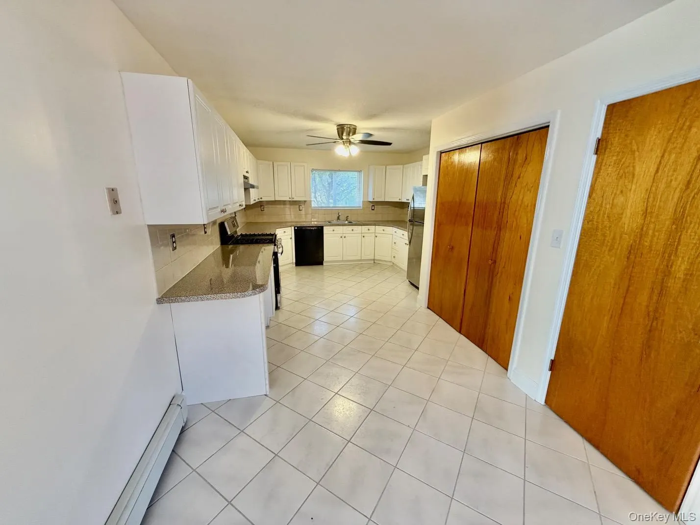 Kitchen featuring light tile patterned floors, white cabinetry, a baseboard heating unit, decorative backsplash, and stainless steel appliances Kitchen featuring light tile patterned floors, white cabinetry, a baseboard heating unit, decorative backsplash, and stainless steel appliances