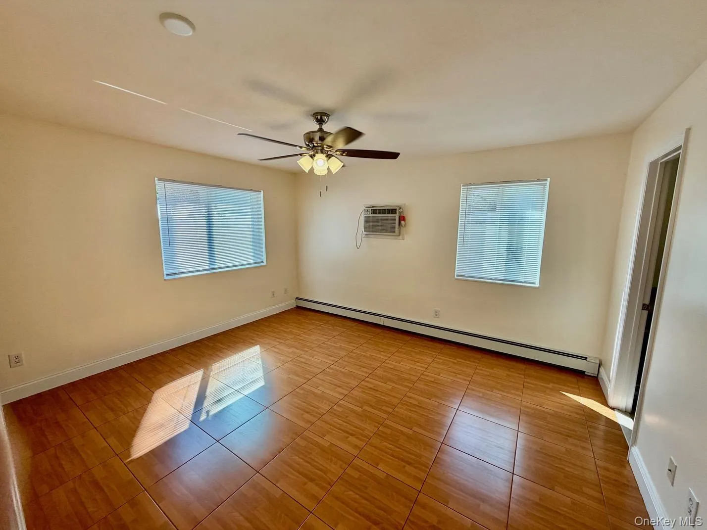 Spare room with a baseboard heating unit, a wall mounted AC, light tile patterned floors, and ceiling fan Spare room with a baseboard heating unit, a wall mounted AC, light tile patterned floors, and ceiling fan