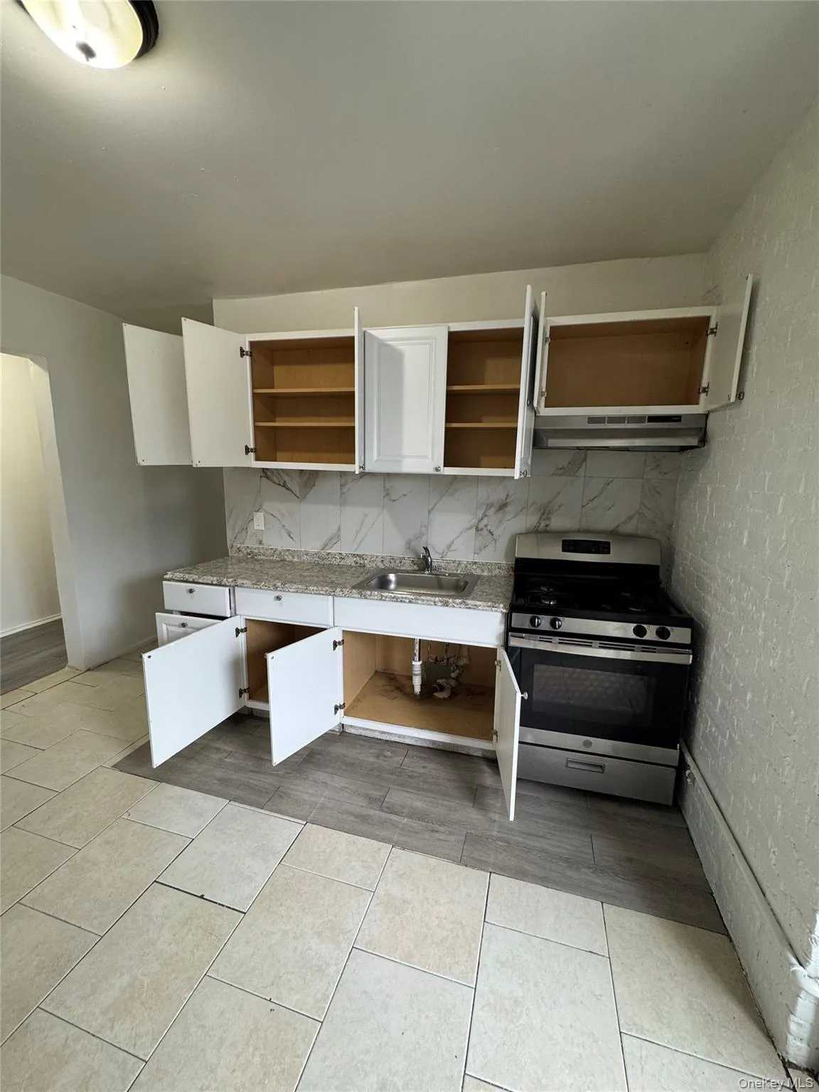 Kitchen with stainless steel gas range, backsplash, light tile patterned flooring, under cabinet range hood, and white cabinets Kitchen with stainless steel gas range, backsplash, light tile patterned flooring, under cabinet range hood, and white cabinets