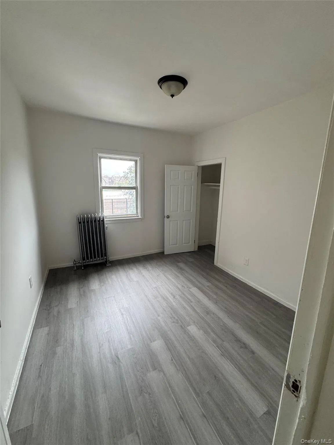 Unfurnished bedroom featuring wood finished floors, radiator, and a closet Unfurnished bedroom featuring wood finished floors, radiator, and a closet