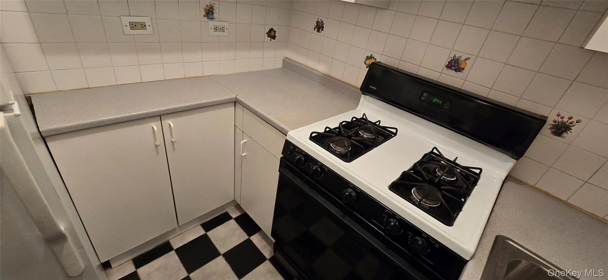Kitchen featuring gas stove, white cabinetry, light countertops, tile patterned floors, and backsplash Kitchen featuring gas stove, white cabinetry, light countertops, tile patterned floors, and backsplash
