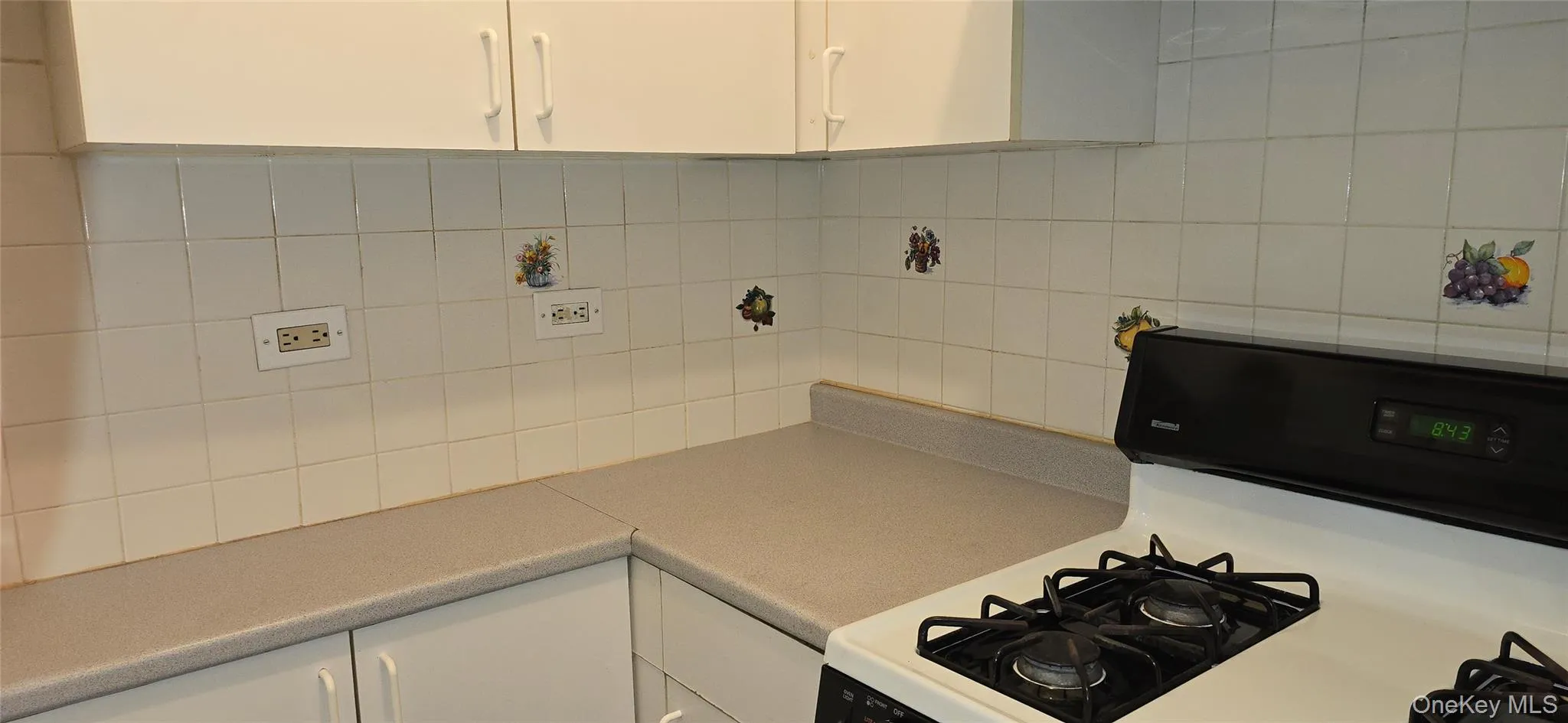 Kitchen with black range with gas cooktop, white cabinets, light countertops, and backsplash Kitchen with black range with gas cooktop, white cabinets, light countertops, and backsplash
