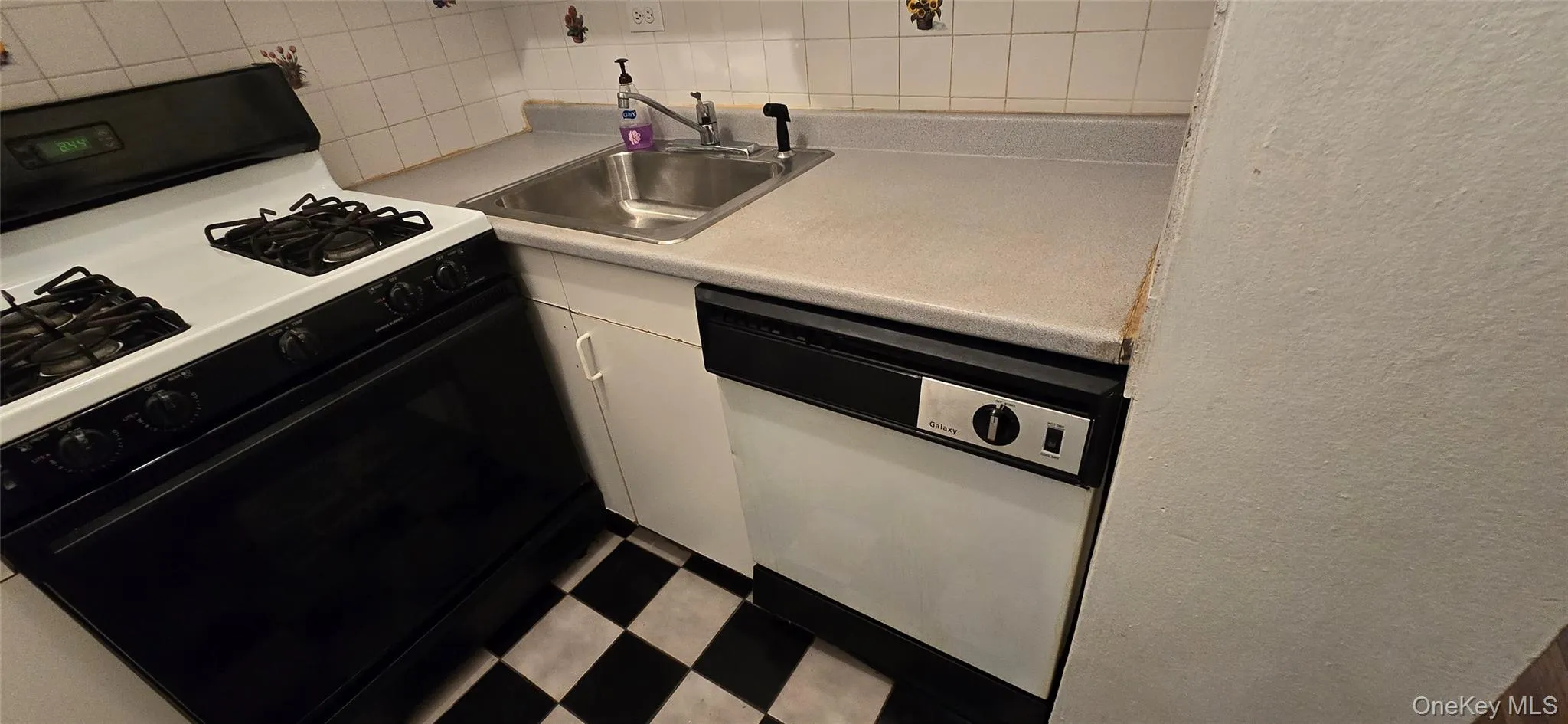 Kitchen with black range with gas stovetop, white dishwasher, white cabinets, light countertops, and decorative backsplash Kitchen with black range with gas stovetop, white dishwasher, white cabinets, light countertops, and decorative backsplash