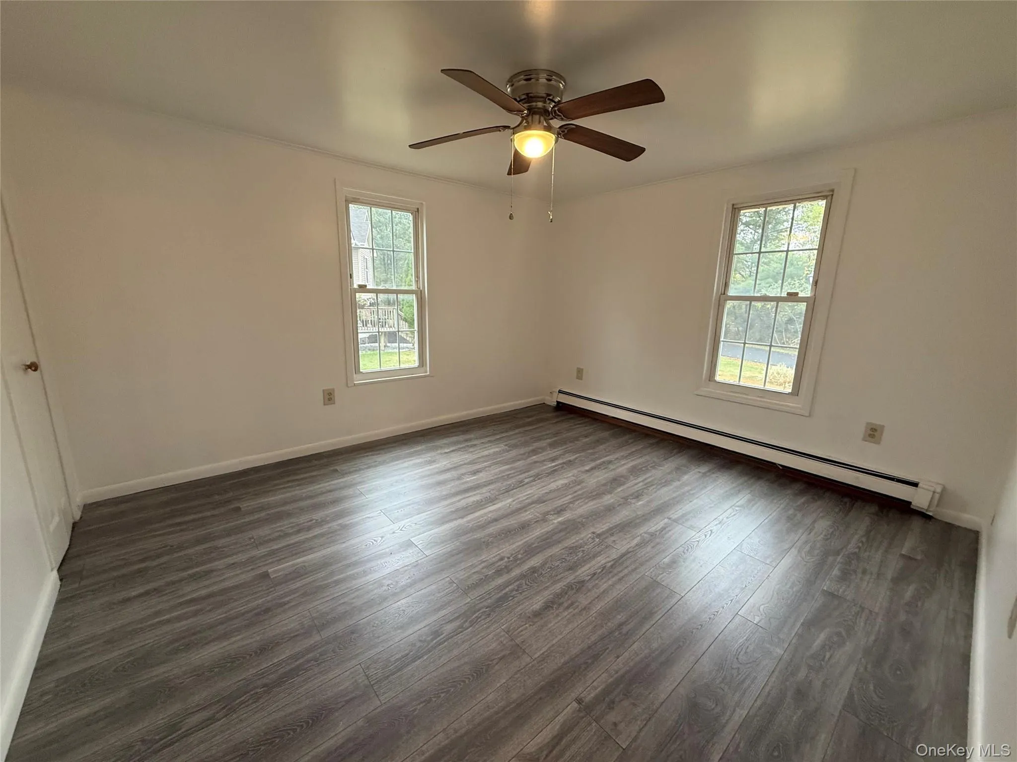 Unfurnished room featuring baseboard heating, dark wood-type flooring, and a ceiling fan Unfurnished room featuring baseboard heating, dark wood-type flooring, and a ceiling fan
