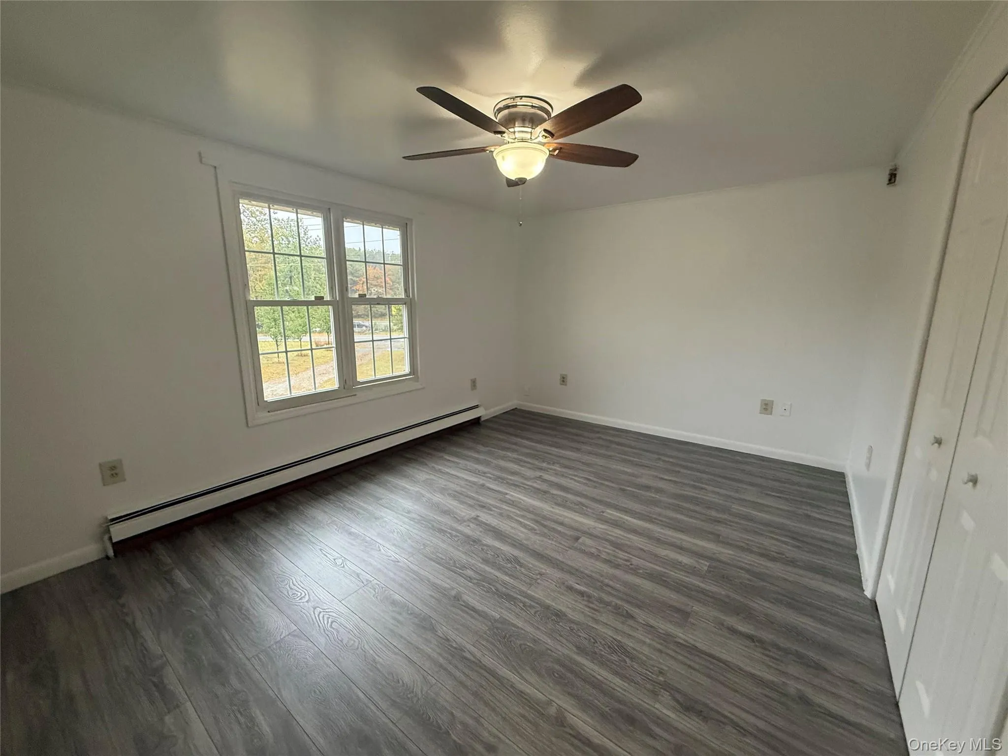 Unfurnished bedroom featuring dark wood finished floors, a baseboard radiator, and a ceiling fan Unfurnished bedroom featuring dark wood finished floors, a baseboard radiator, and a ceiling fan