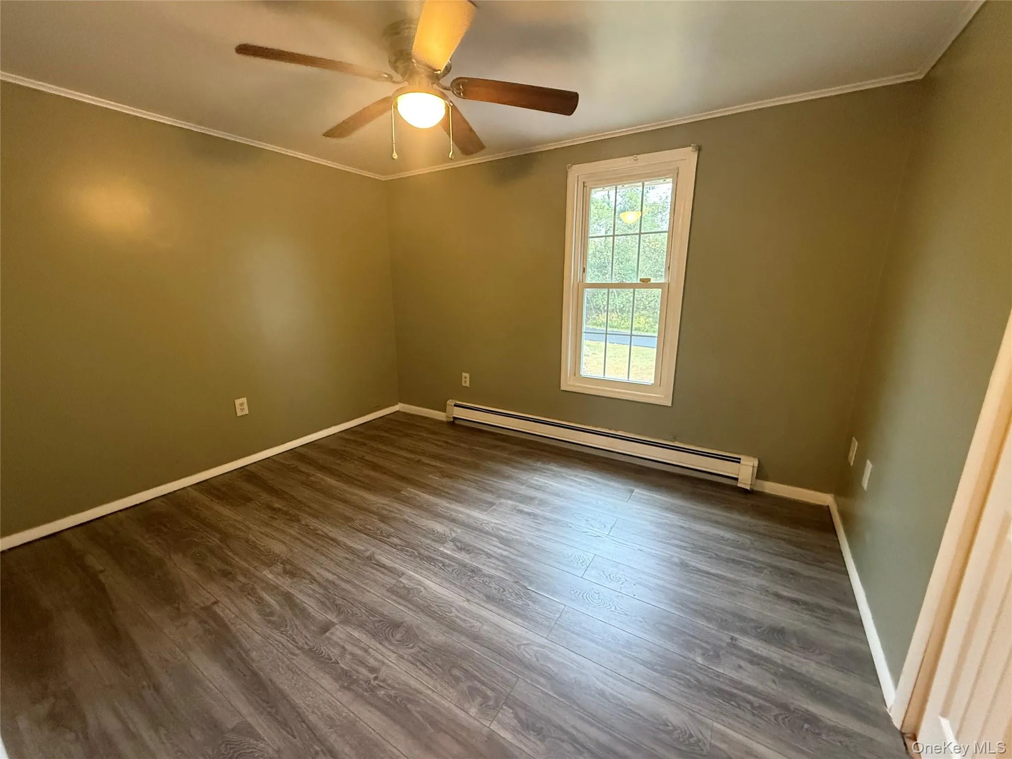 Empty room with crown molding, a baseboard heating unit, dark wood-type flooring, and ceiling fan Empty room with crown molding, a baseboard heating unit, dark wood-type flooring, and ceiling fan