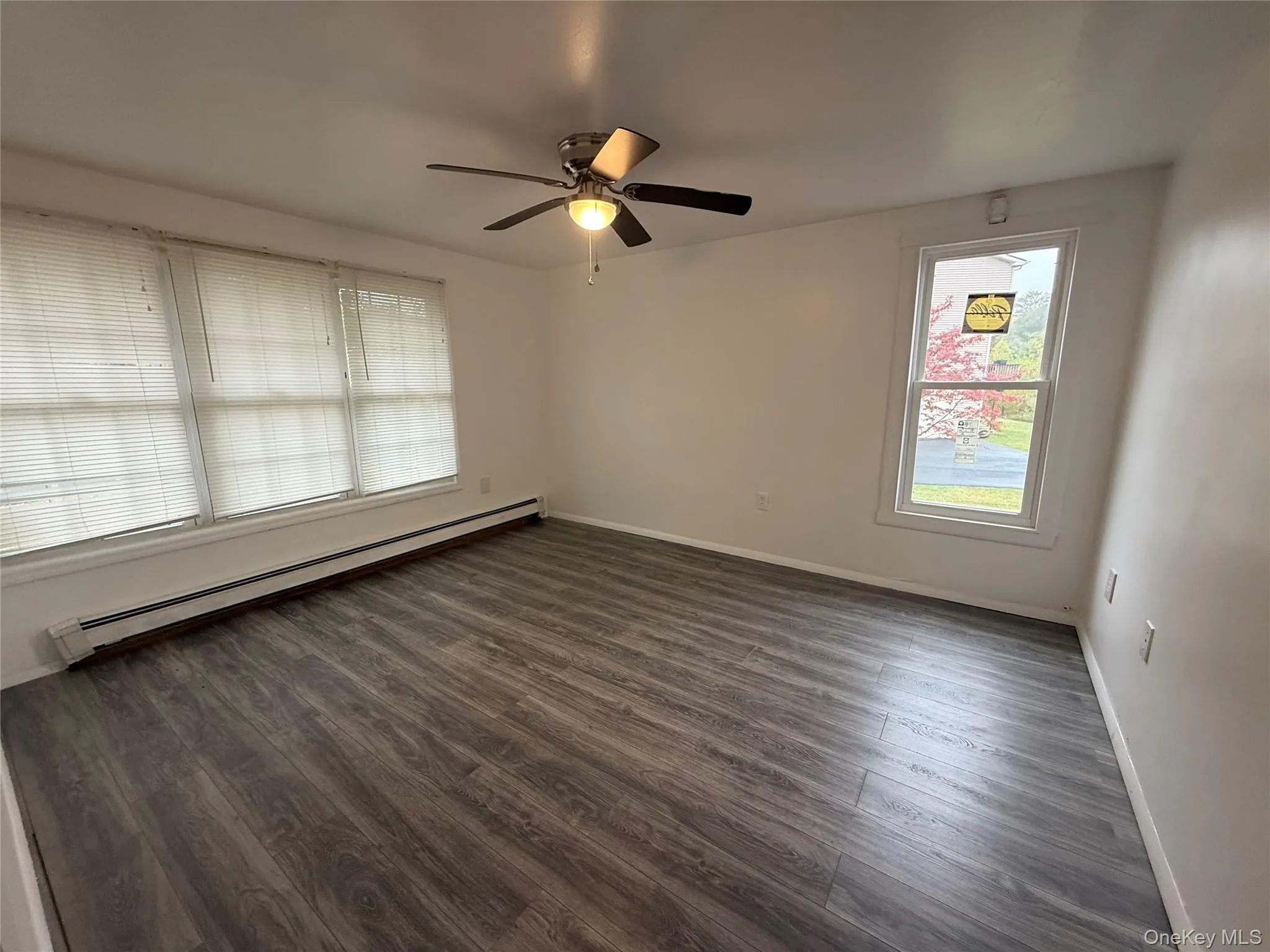 Empty room with baseboard heating, dark wood-type flooring, and ceiling fan Empty room with baseboard heating, dark wood-type flooring, and ceiling fan