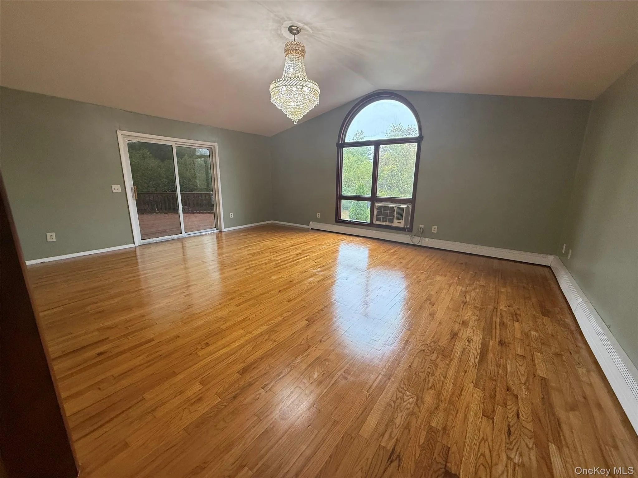 Unfurnished room featuring light wood-type flooring, a chandelier, vaulted ceiling, and a baseboard heating unit Unfurnished room featuring light wood-type flooring, a chandelier, vaulted ceiling, and a baseboard heating unit