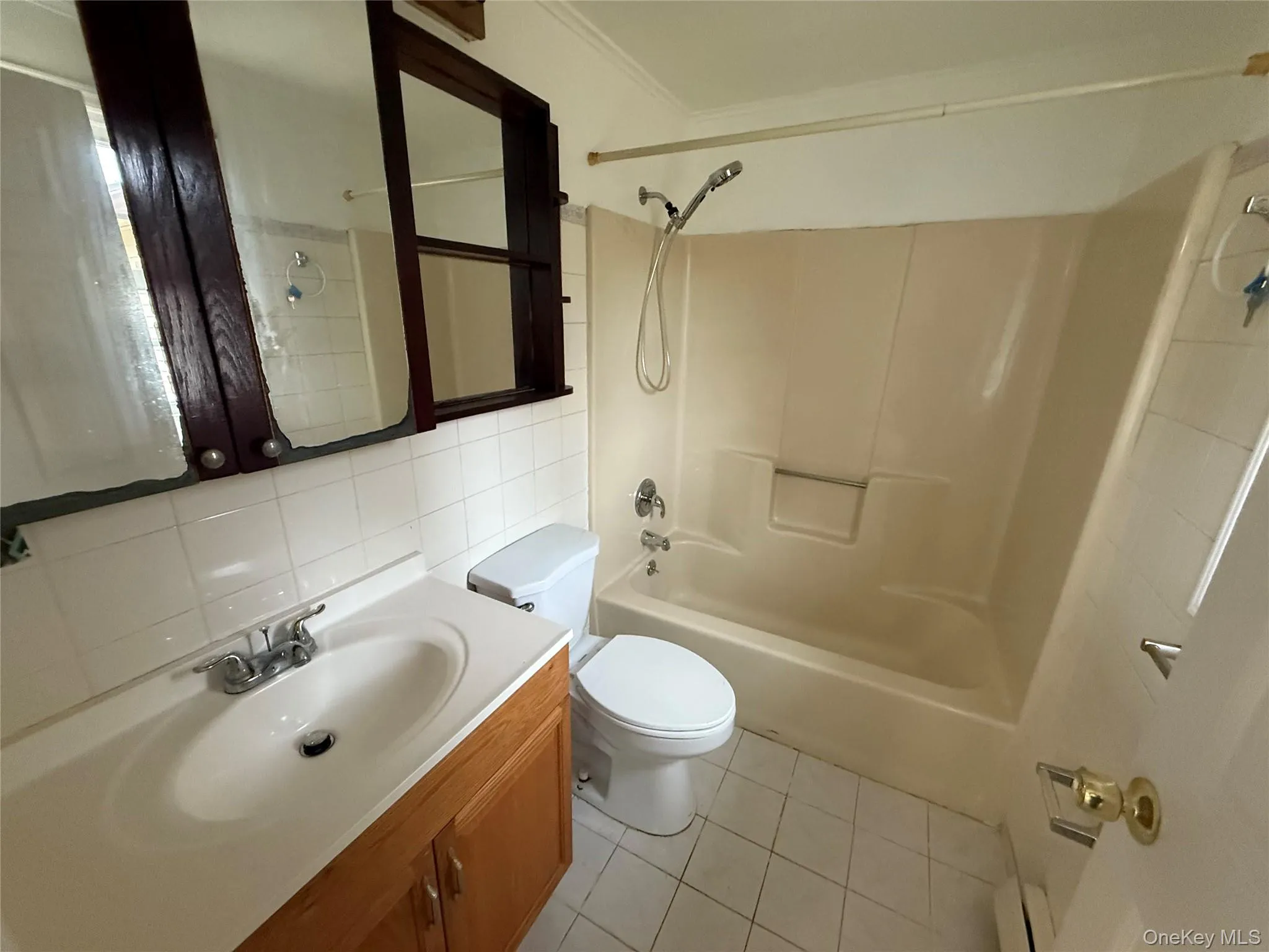 Bathroom featuring shower / tub combination, tile walls, vanity, light tile patterned floors, and ornamental molding Bathroom featuring shower / tub combination, tile walls, vanity, light tile patterned floors, and ornamental molding