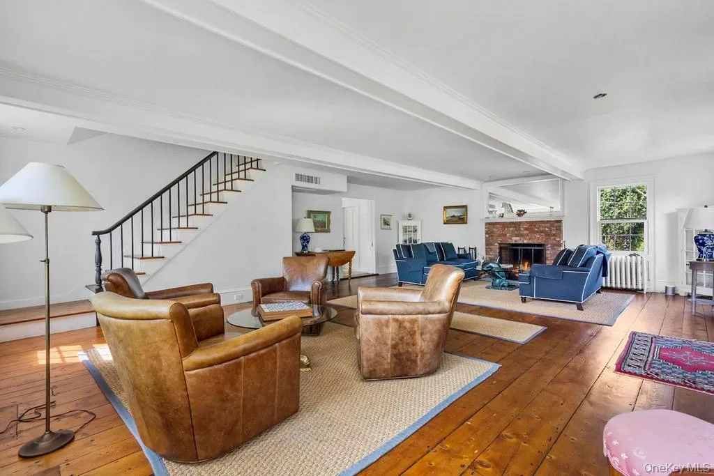 Living area with beam ceiling, hardwood / wood-style floors, stairway, a brick fireplace, and radiator Living area with beam ceiling, hardwood / wood-style floors, stairway, a brick fireplace, and radiator