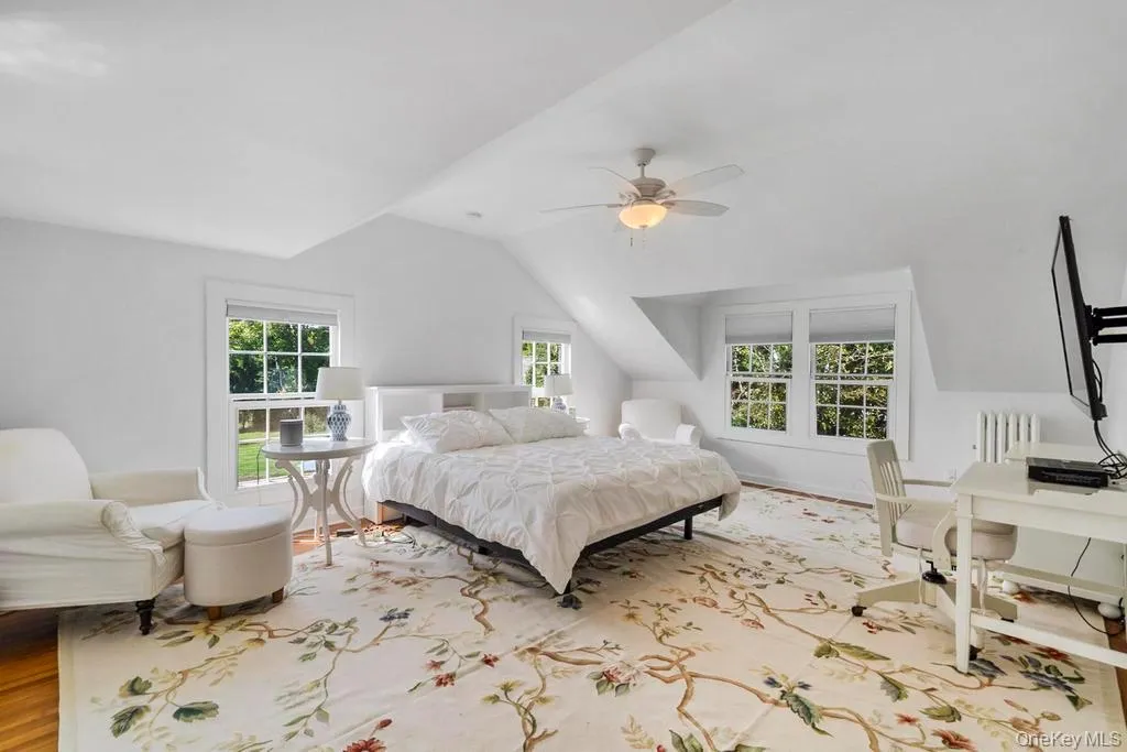 Bedroom featuring vaulted ceiling, multiple windows, wood finished floors, radiator heating unit, and a ceiling fan Bedroom featuring vaulted ceiling, multiple windows, wood finished floors, radiator heating unit, and a ceiling fan