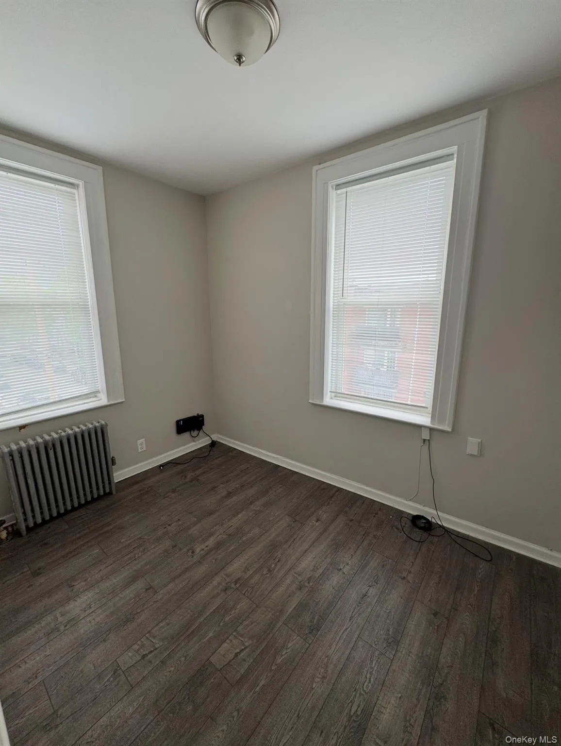 Unfurnished room with radiator and dark wood-style flooring Unfurnished room with radiator and dark wood-style flooring