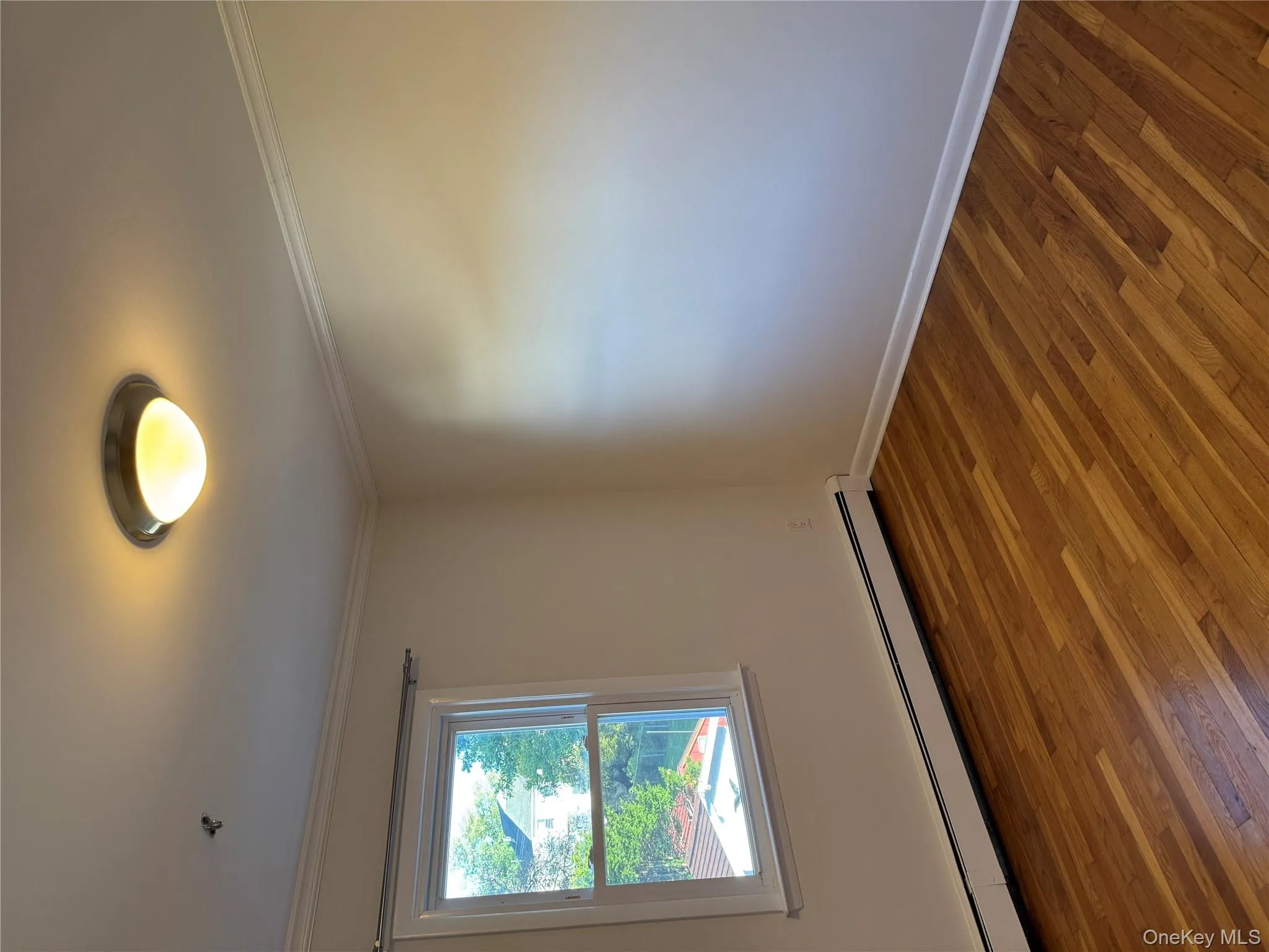 Empty room with baseboard heating, wood finished floors, and ornamental molding Empty room with baseboard heating, wood finished floors, and ornamental molding