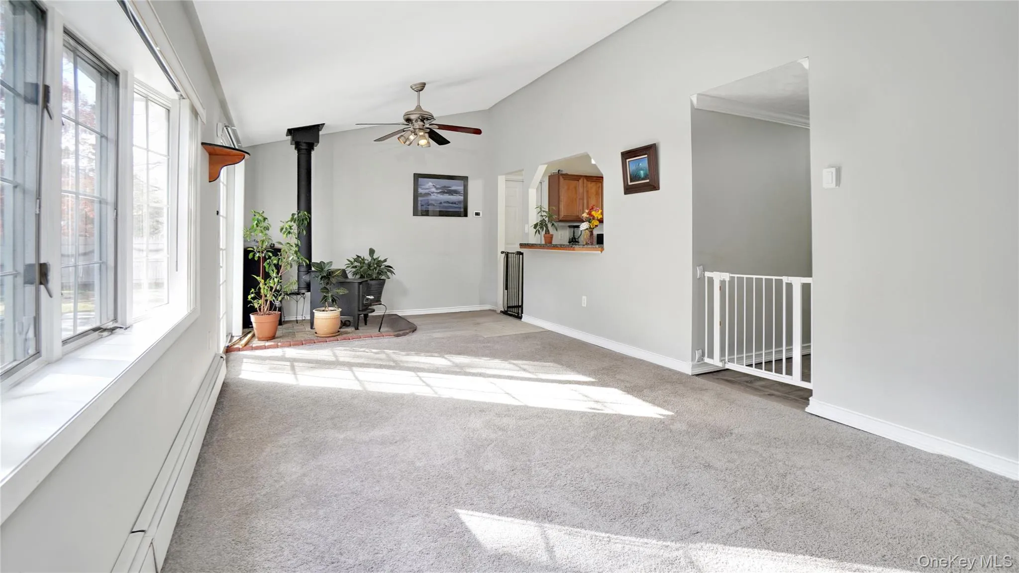 Spare room featuring a wood stove, a baseboard heating unit, lofted ceiling, light carpet, and ceiling fan Spare room featuring a wood stove, a baseboard heating unit, lofted ceiling, light carpet, and ceiling fan