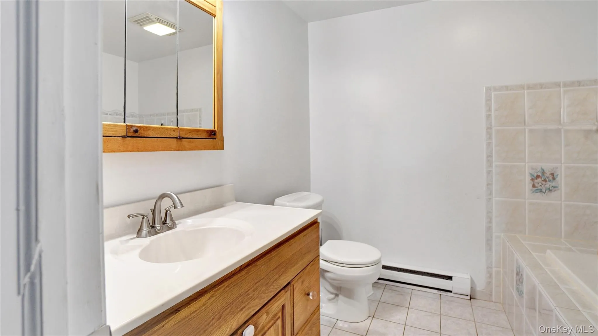 Bathroom with light tile patterned floors, a baseboard radiator, vanity, and tiled tub Bathroom with light tile patterned floors, a baseboard radiator, vanity, and tiled tub