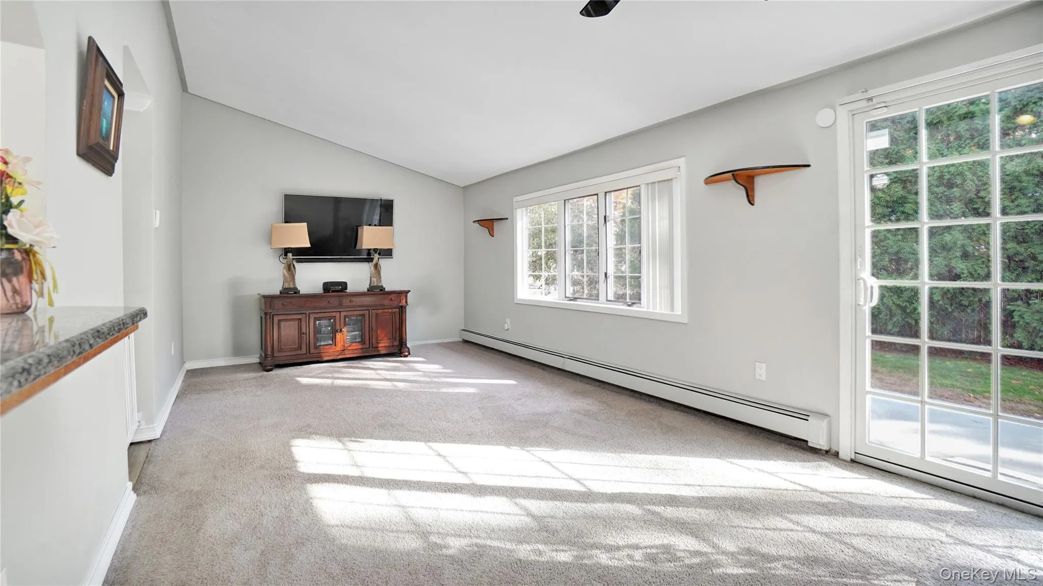 Unfurnished living room featuring a baseboard radiator, lofted ceiling, and light carpet Unfurnished living room featuring a baseboard radiator, lofted ceiling, and light carpet