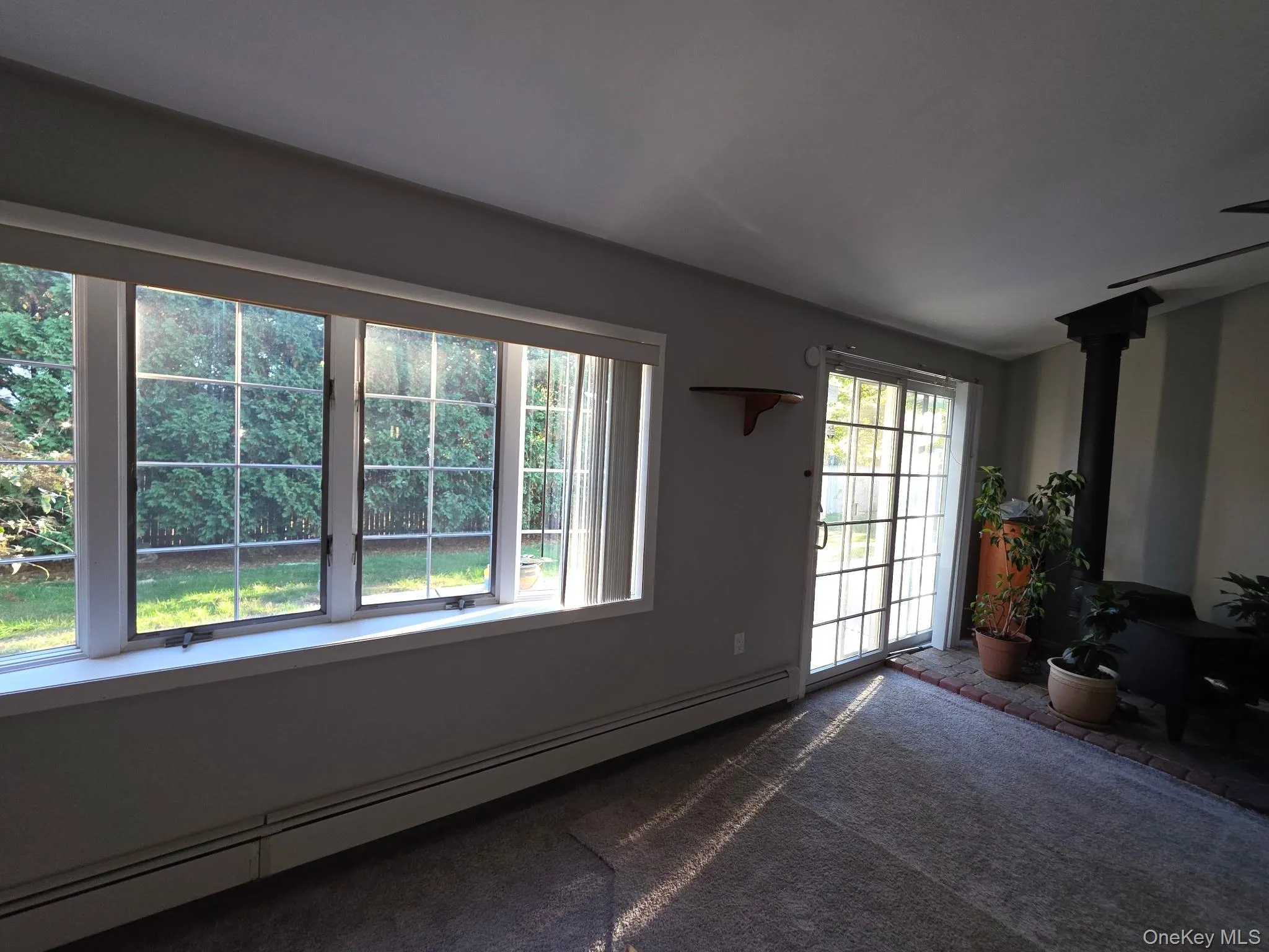 Carpeted living room featuring a baseboard heating unit and a wood stove Carpeted living room featuring a baseboard heating unit and a wood stove