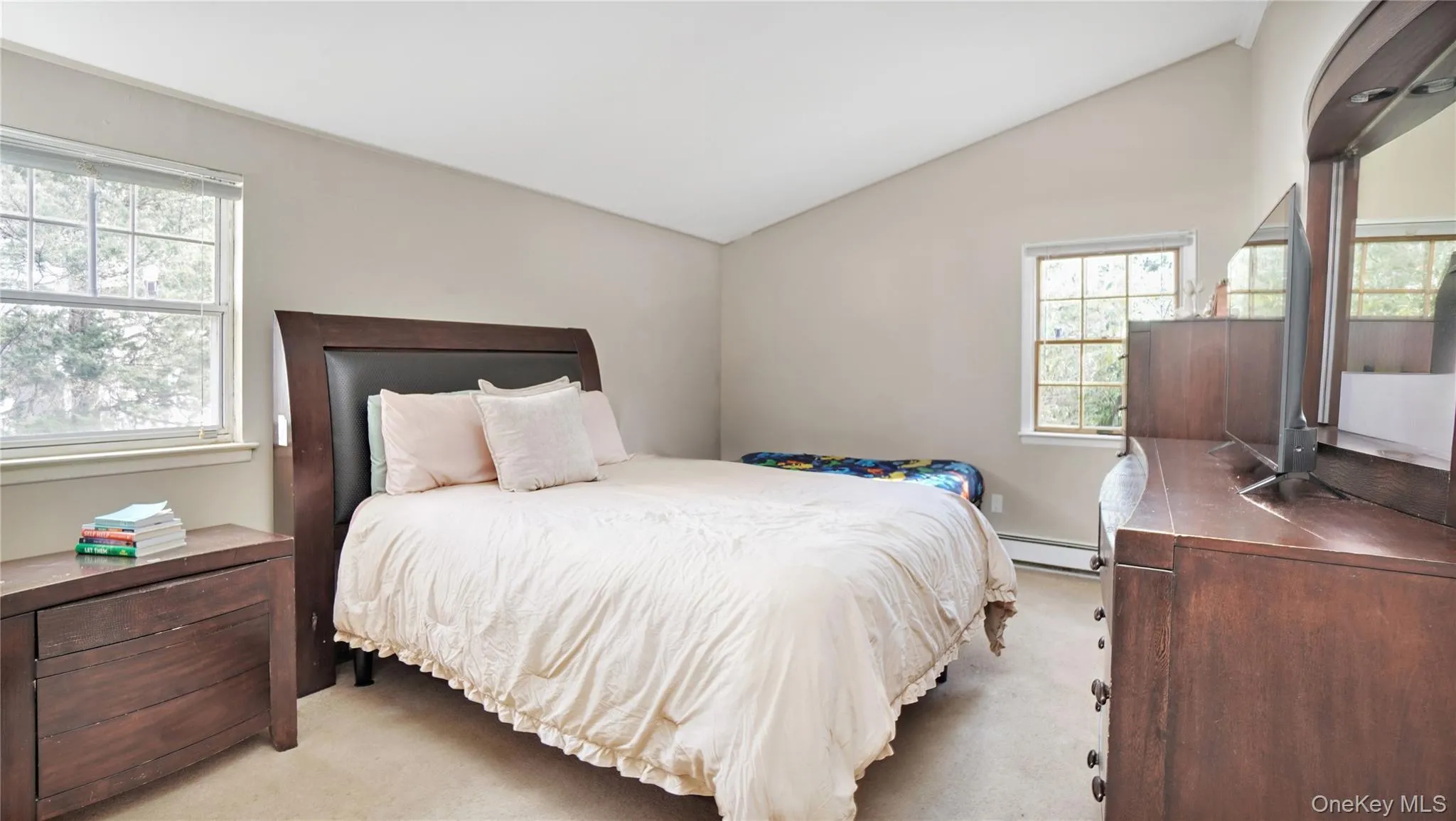 Bedroom featuring light carpet, vaulted ceiling, multiple windows, and a baseboard heating unit Bedroom featuring light carpet, vaulted ceiling, multiple windows, and a baseboard heating unit