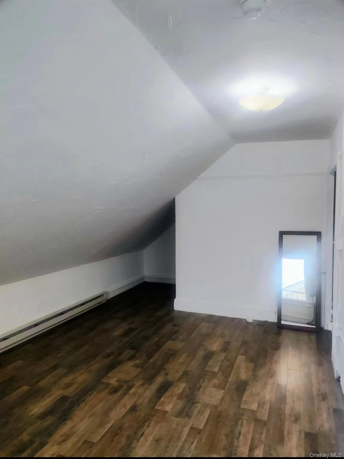 Additional living space with a baseboard heating unit, lofted ceiling, and dark wood-style floors Additional living space with a baseboard heating unit, lofted ceiling, and dark wood-style floors