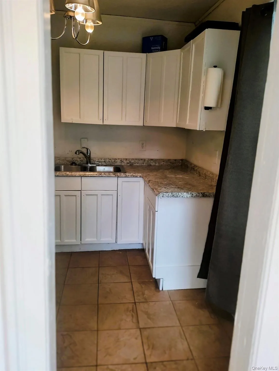 Kitchen with white cabinets, tile patterned floors, pendant lighting, a chandelier, and light countertops Kitchen with white cabinets, tile patterned floors, pendant lighting, a chandelier, and light countertops