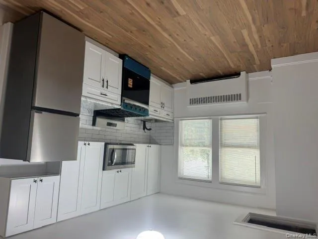 Kitchen with refrigerator, white cabinets, stove, radiator heating unit, and tasteful backsplash Kitchen with refrigerator, white cabinets, stove, radiator heating unit, and tasteful backsplash