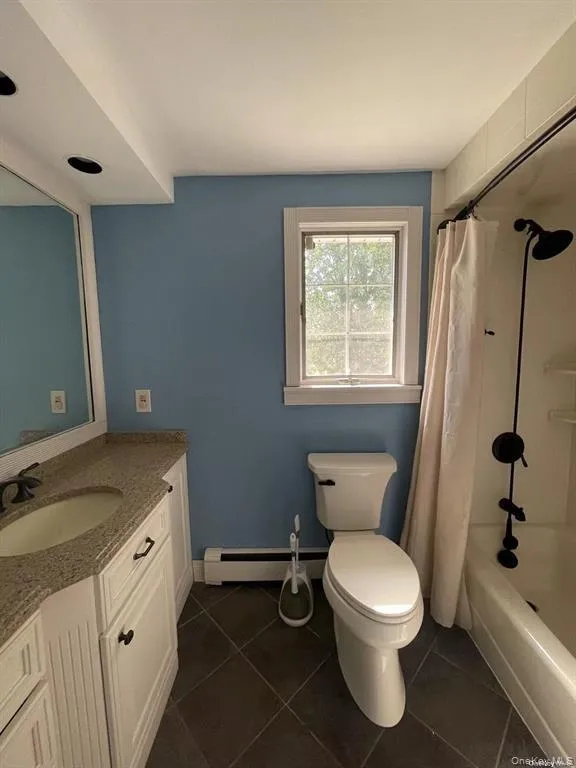 Bathroom with vanity, shower / bathtub combination with curtain, dark tile patterned floors, and a baseboard radiator Bathroom with vanity, shower / bathtub combination with curtain, dark tile patterned floors, and a baseboard radiator
