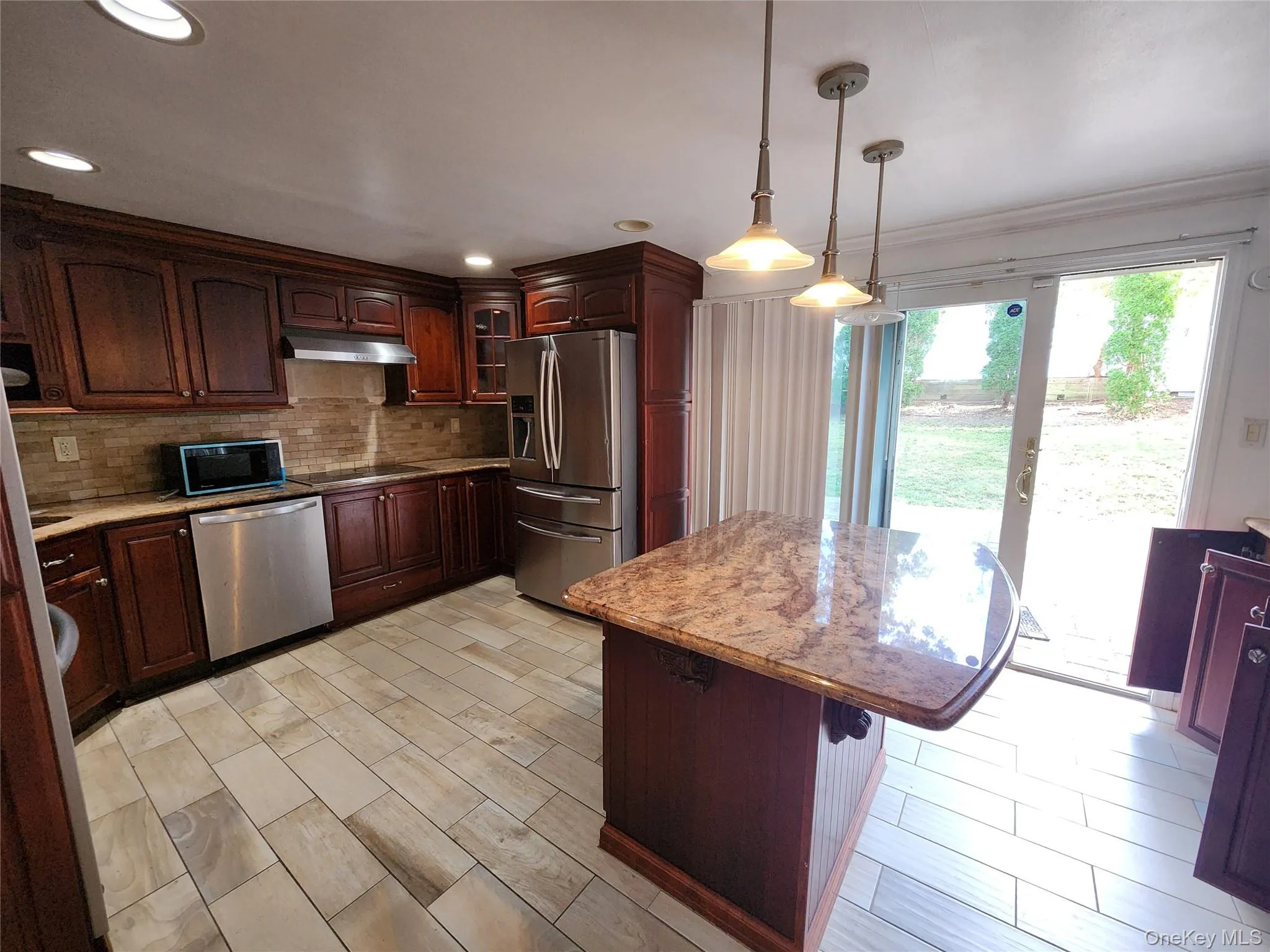 Kitchen with stainless steel appliances, decorative backsplash, decorative light fixtures, a kitchen island, and a kitchen bar Kitchen with stainless steel appliances, decorative backsplash, decorative light fixtures, a kitchen island, and a kitchen bar