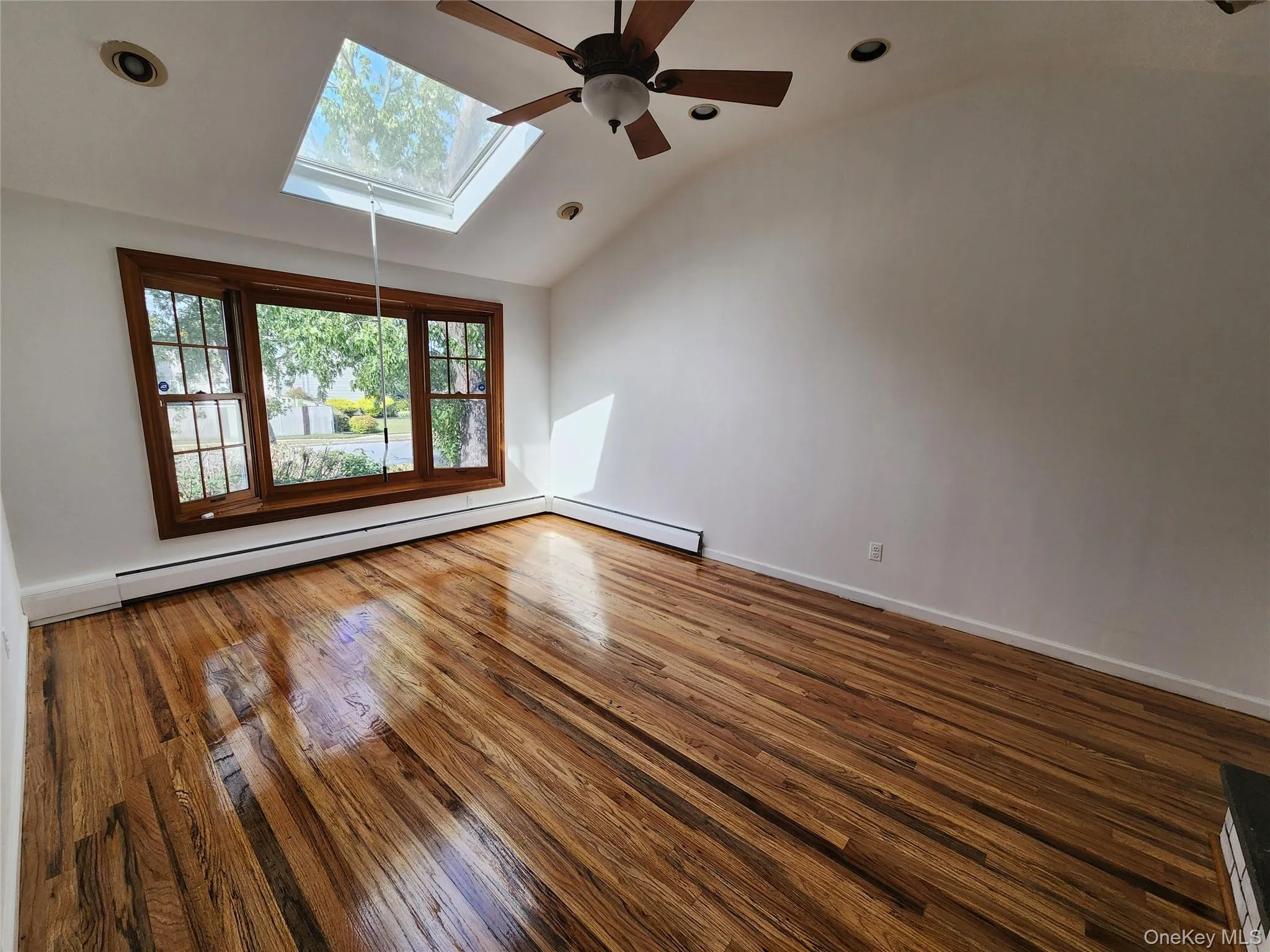 Unfurnished room with hardwood / wood-style floors, lofted ceiling, baseboard heating, recessed lighting, and a skylight Unfurnished room with hardwood / wood-style floors, lofted ceiling, baseboard heating, recessed lighting, and a skylight