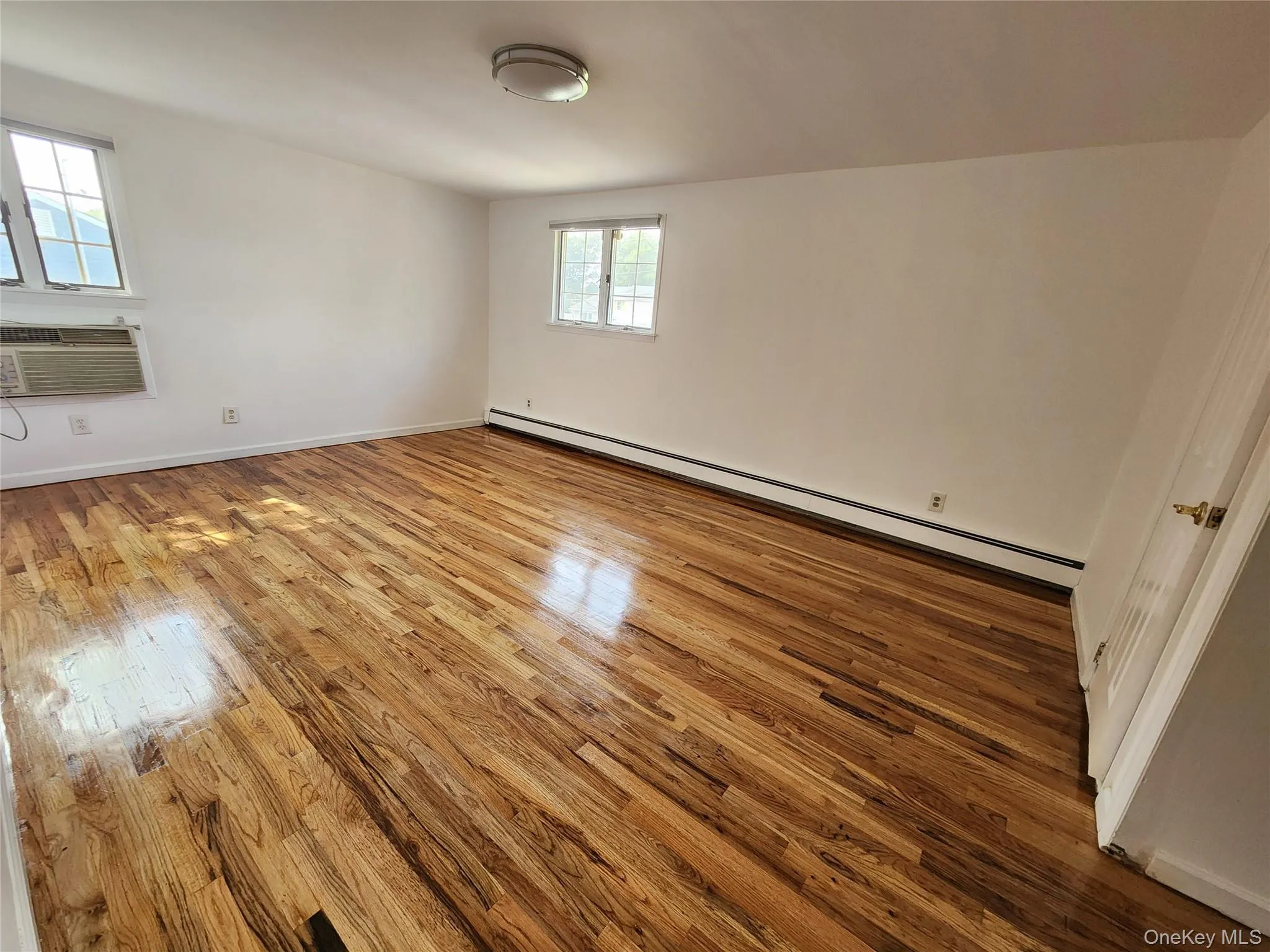 Unfurnished room featuring baseboard heating and light wood finished floors Unfurnished room featuring baseboard heating and light wood finished floors