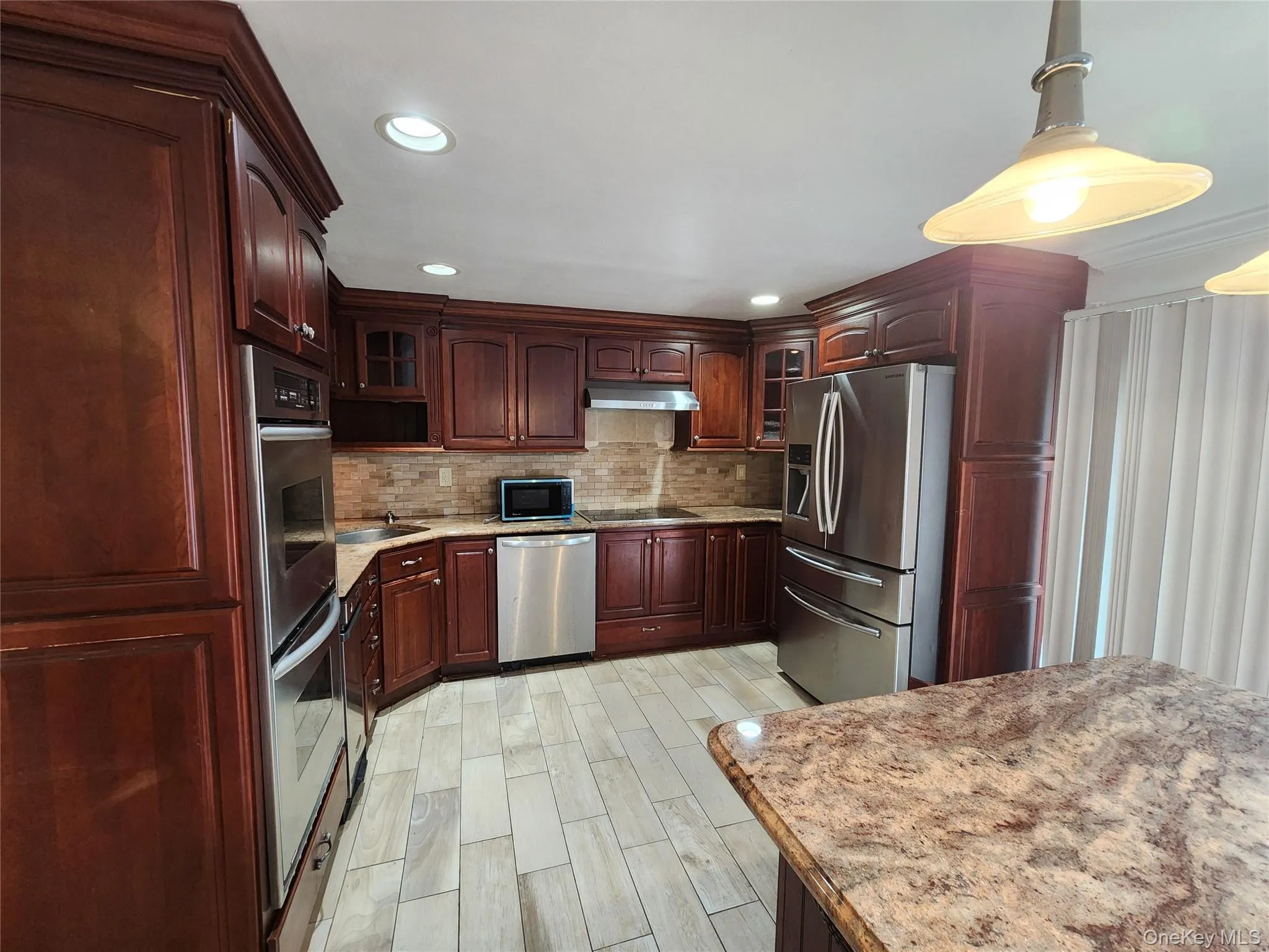 Kitchen featuring black appliances, glass insert cabinets, tasteful backsplash, recessed lighting, and light stone countertops Kitchen featuring black appliances, glass insert cabinets, tasteful backsplash, recessed lighting, and light stone countertops