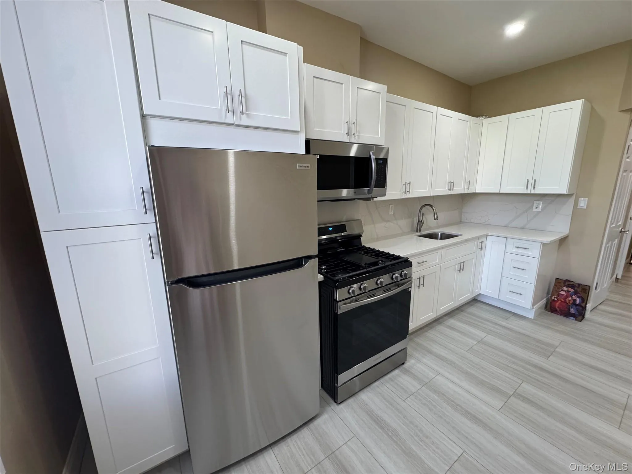 Kitchen with stainless steel appliances, white cabinetry, decorative backsplash, light stone counters, and light wood finished floors Kitchen with stainless steel appliances, white cabinetry, decorative backsplash, light stone counters, and light wood finished floors