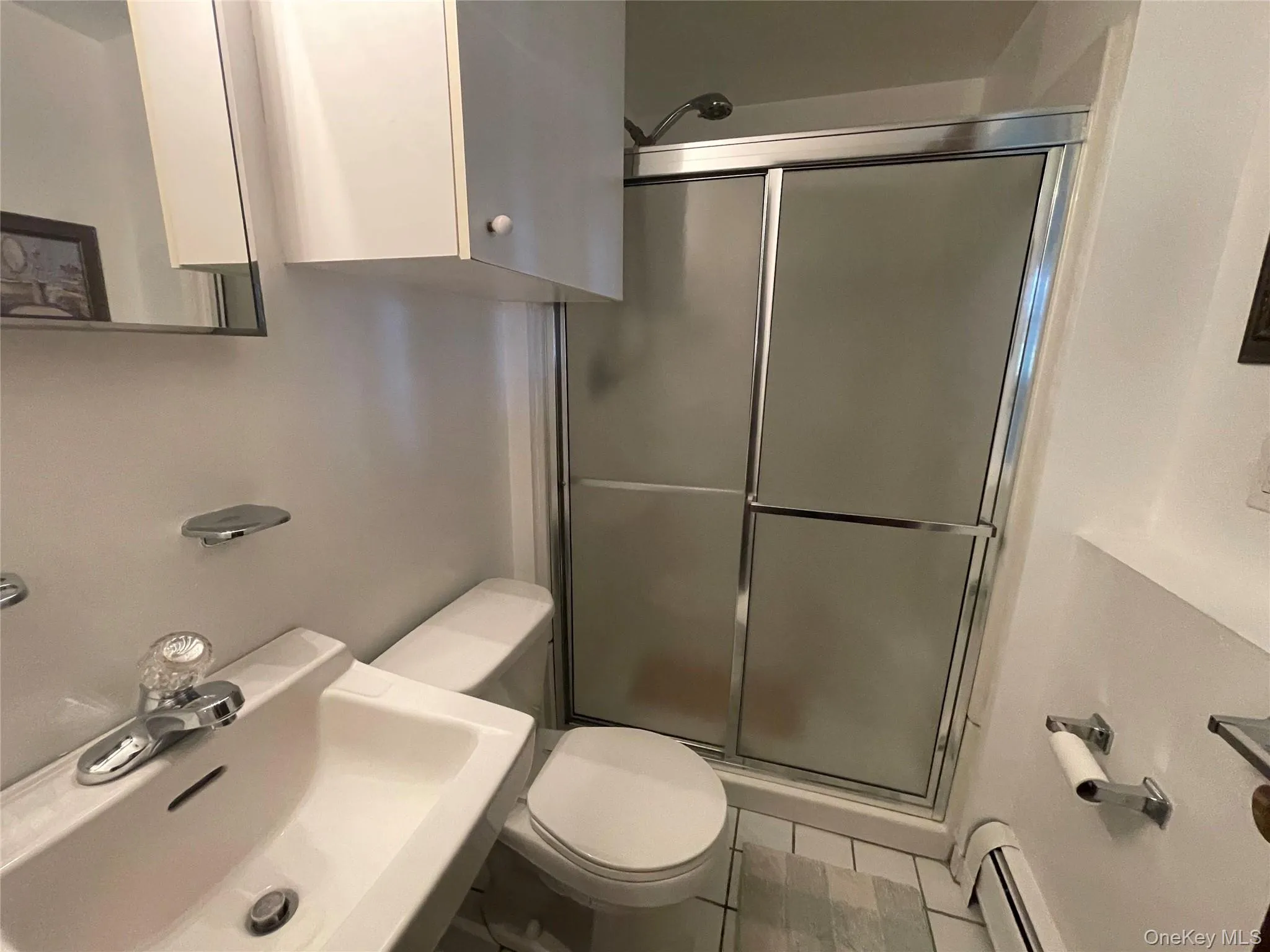 Full bathroom featuring a shower stall, a baseboard heating unit, and light tile patterned flooring Full bathroom featuring a shower stall, a baseboard heating unit, and light tile patterned flooring